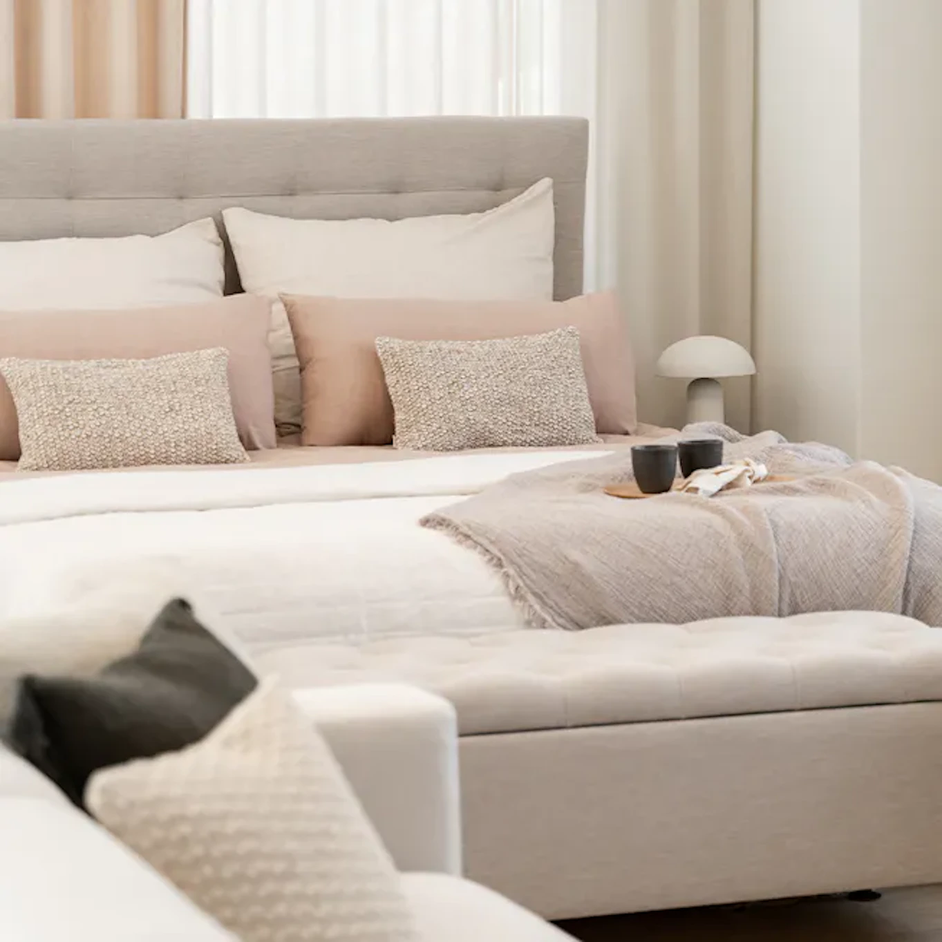 Ljusgrå kontinentalsäng med sänggavel och ljusa sängkläder i ett ljust och medelhavsinspirerat sovrum. 