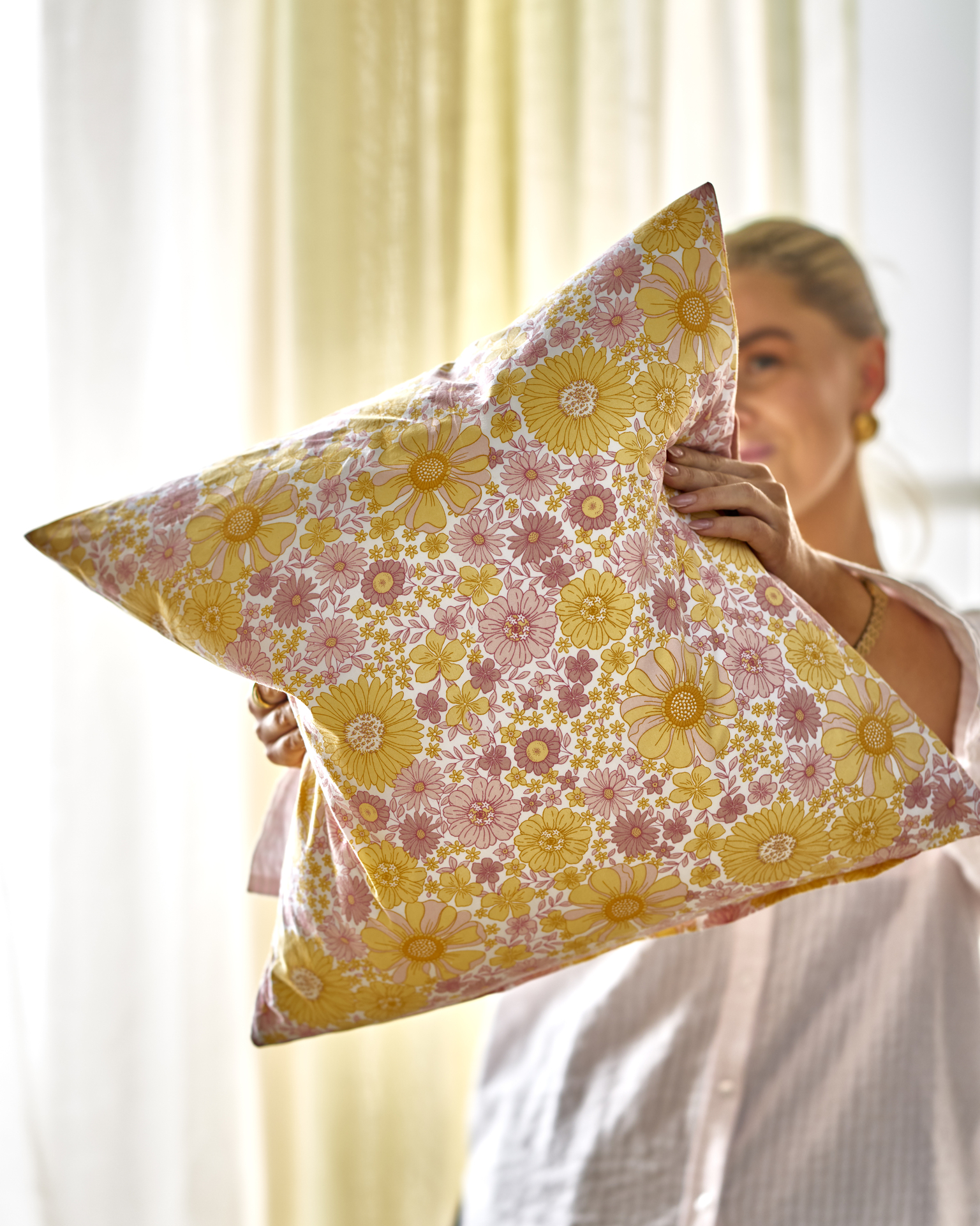 en tjej håller fram en kudde med gula och rosa färger framför sitt ansikte