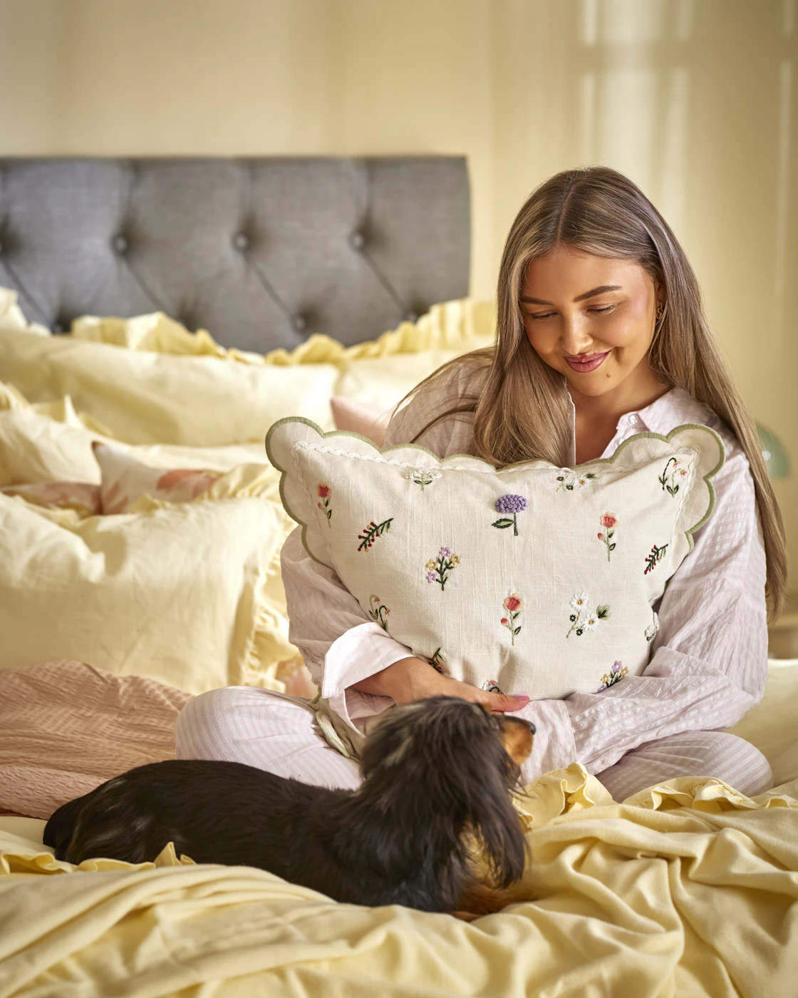 en tjej sitter i en säng med sin hund och kramar en kudde