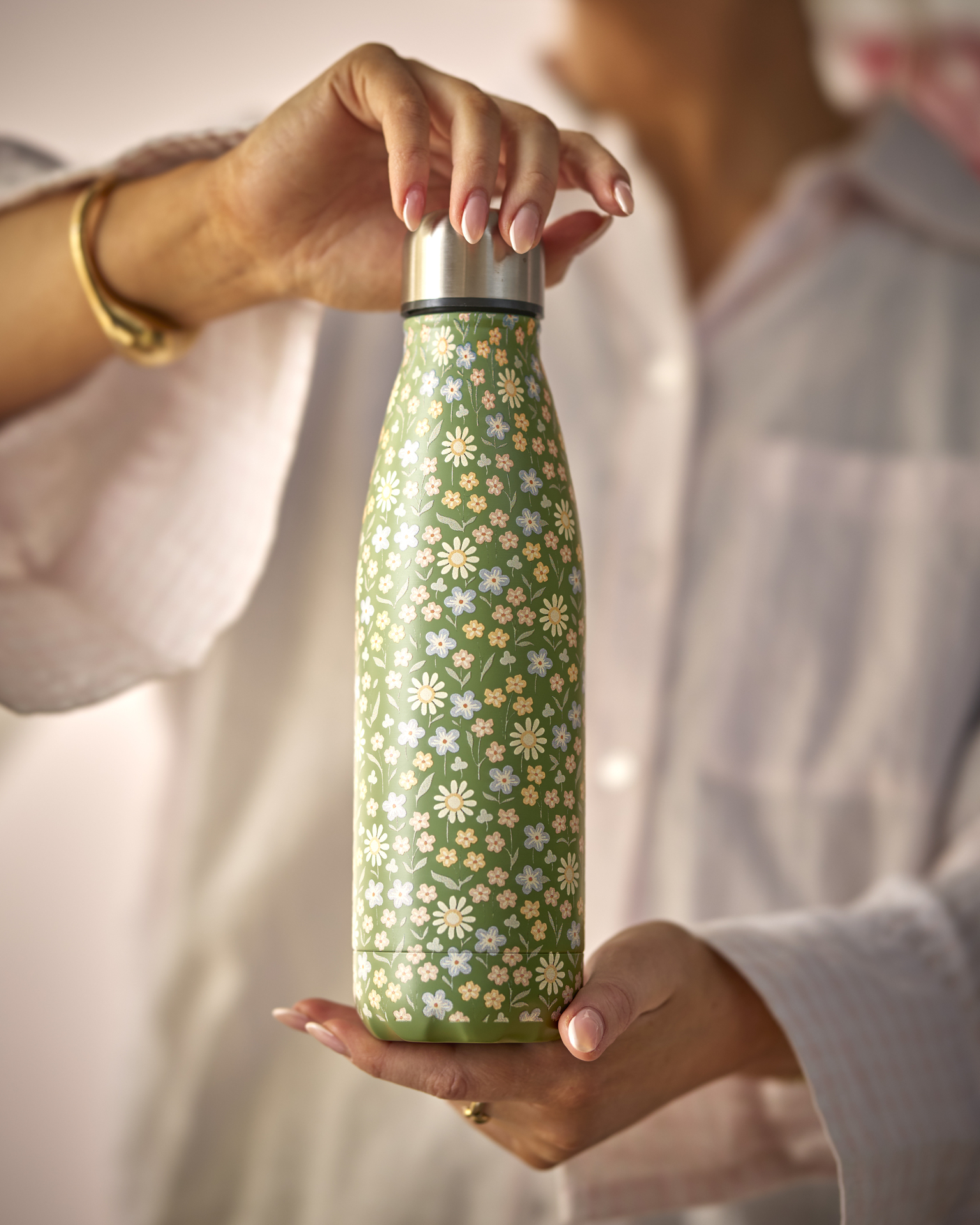 en person håller upp en grönblommig termos