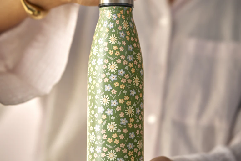 en person håller upp en grönblommig termos