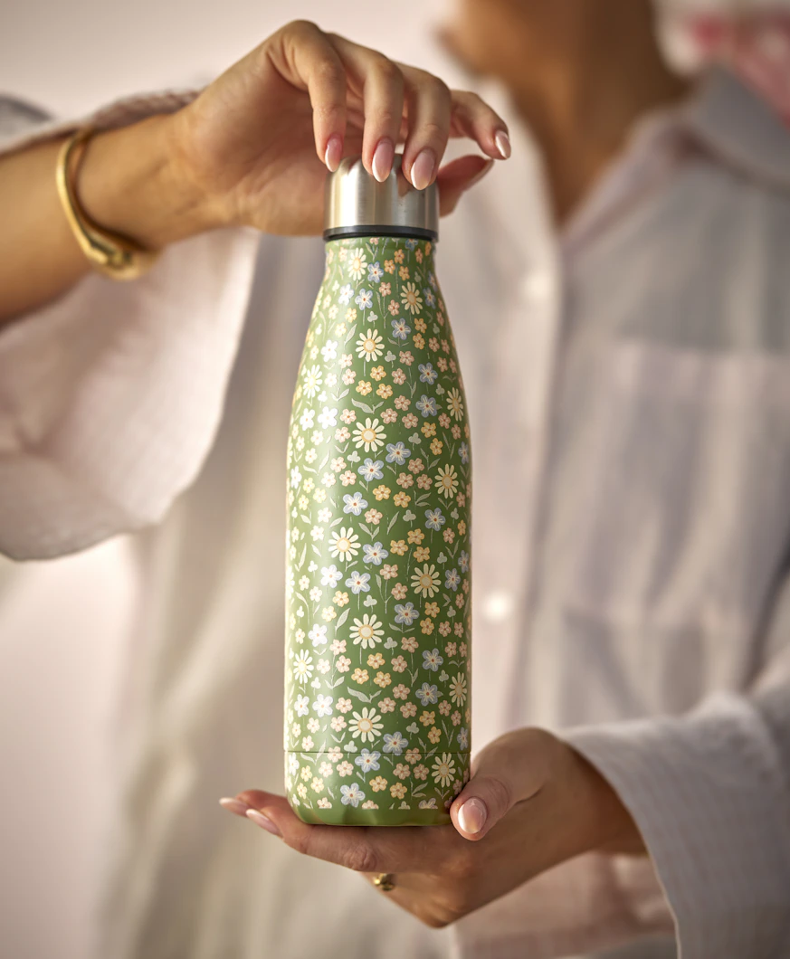 en person håller upp en grönblommig termos