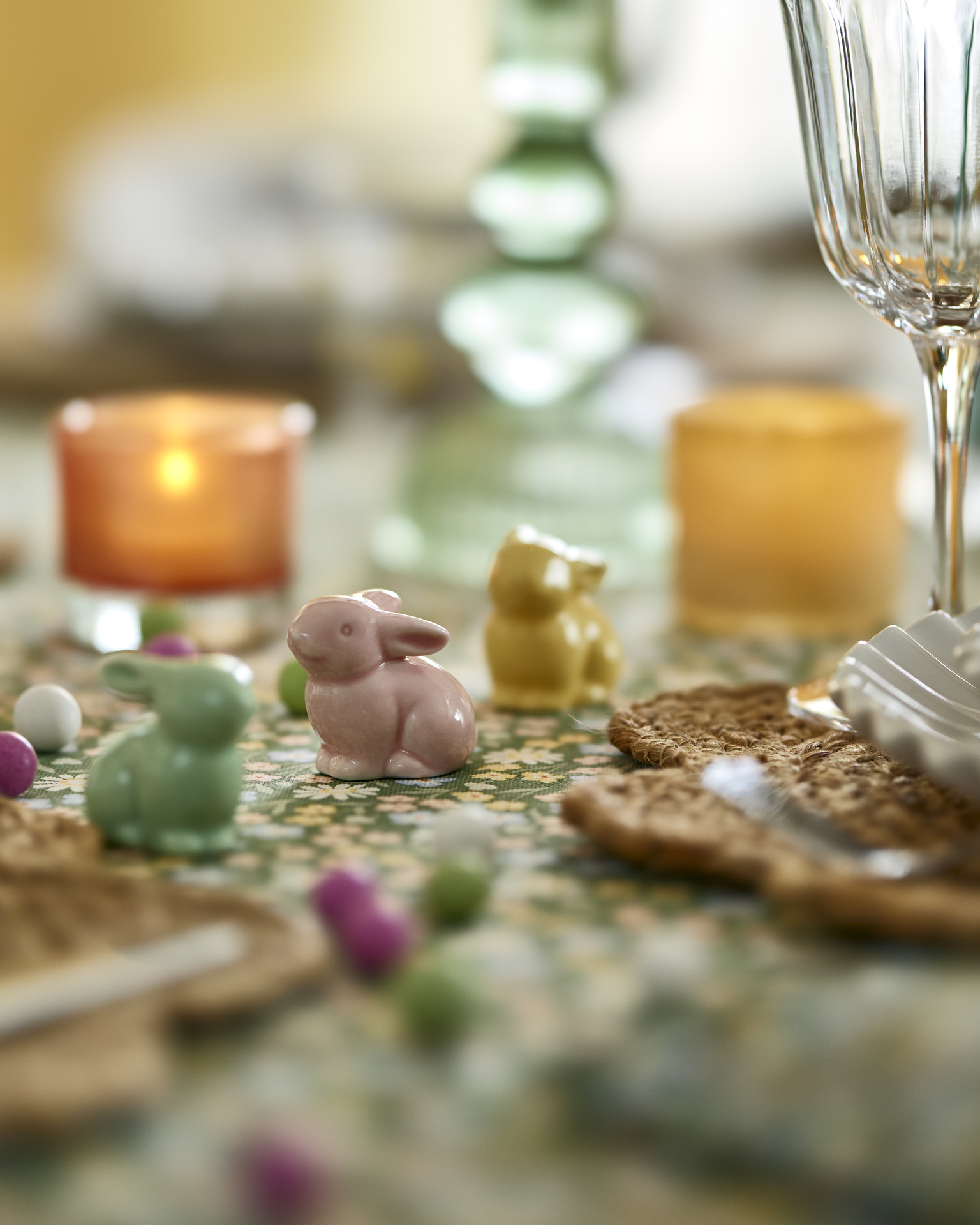 tre små porslinskaniner i grönt, gult och rosa står på ett bord med en grön duk