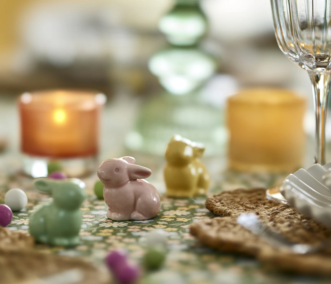 tre små porslinskaniner i grönt, gult och rosa står på ett bord med en grön duk