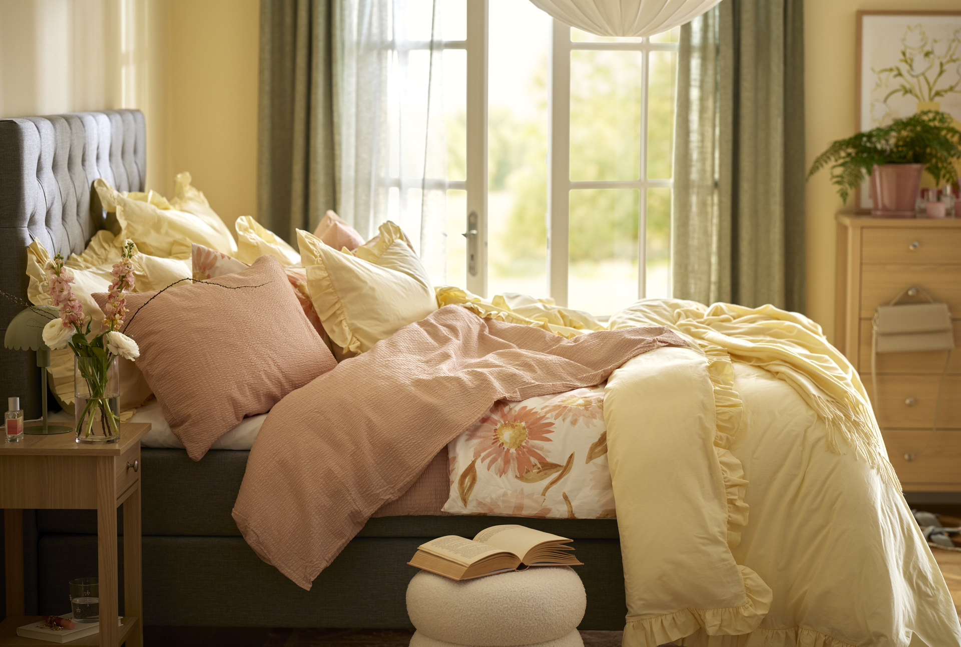 en grå kontinentalsäng står bäddad med gula och rosa påslakan i ett sovrum med gula väggar