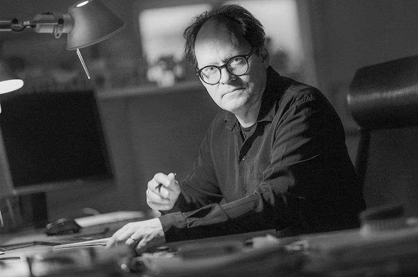 Svartvit bild på designers Jesper Ståhl sittandes med pennan vid ett skrivbord, tillsammans med två frilagda bilder på stolen som Jesper designat som heter Vista.