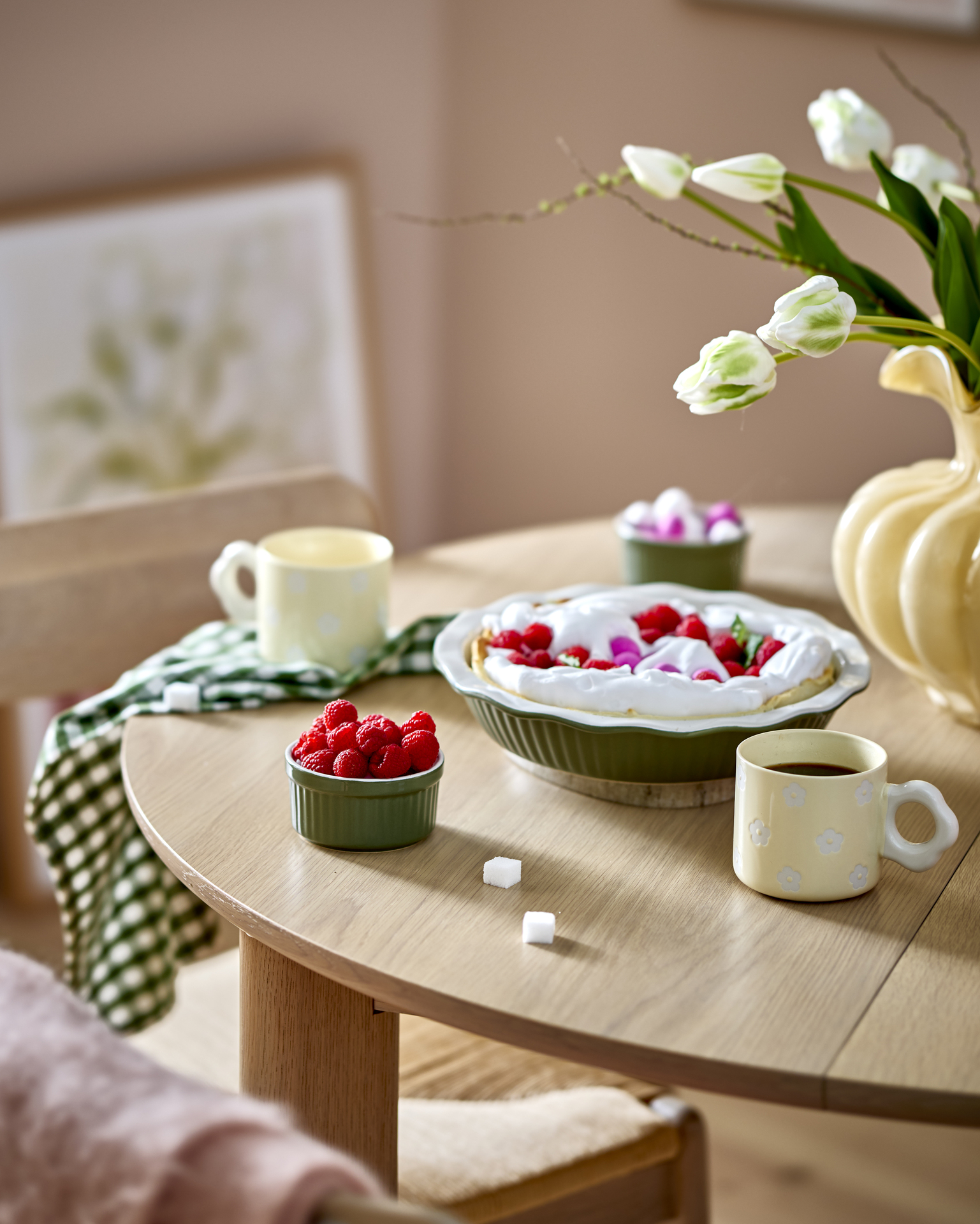 på ett bord i trä står en grön pajform, två gula muggar med blommor på och en liten grön skål med hallon