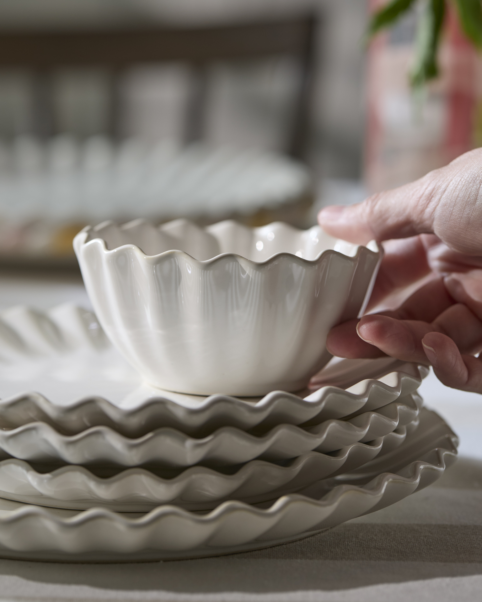 En hand håller i en skål från servisen Shelly, som är travad på tallrikar från samma serie.