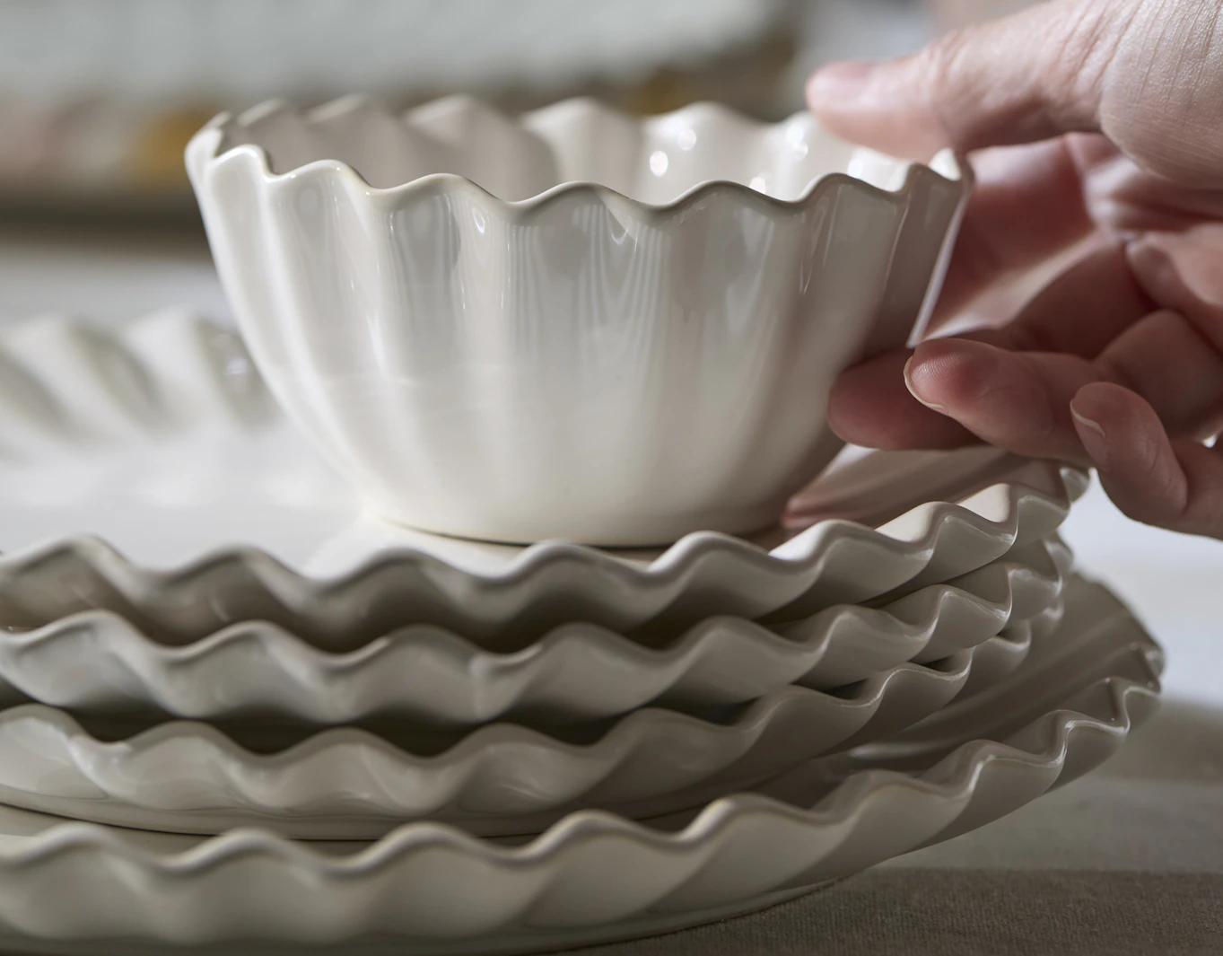 En hand håller i en skål från servisen Shelly, som är travad på tallrikar från samma serie.