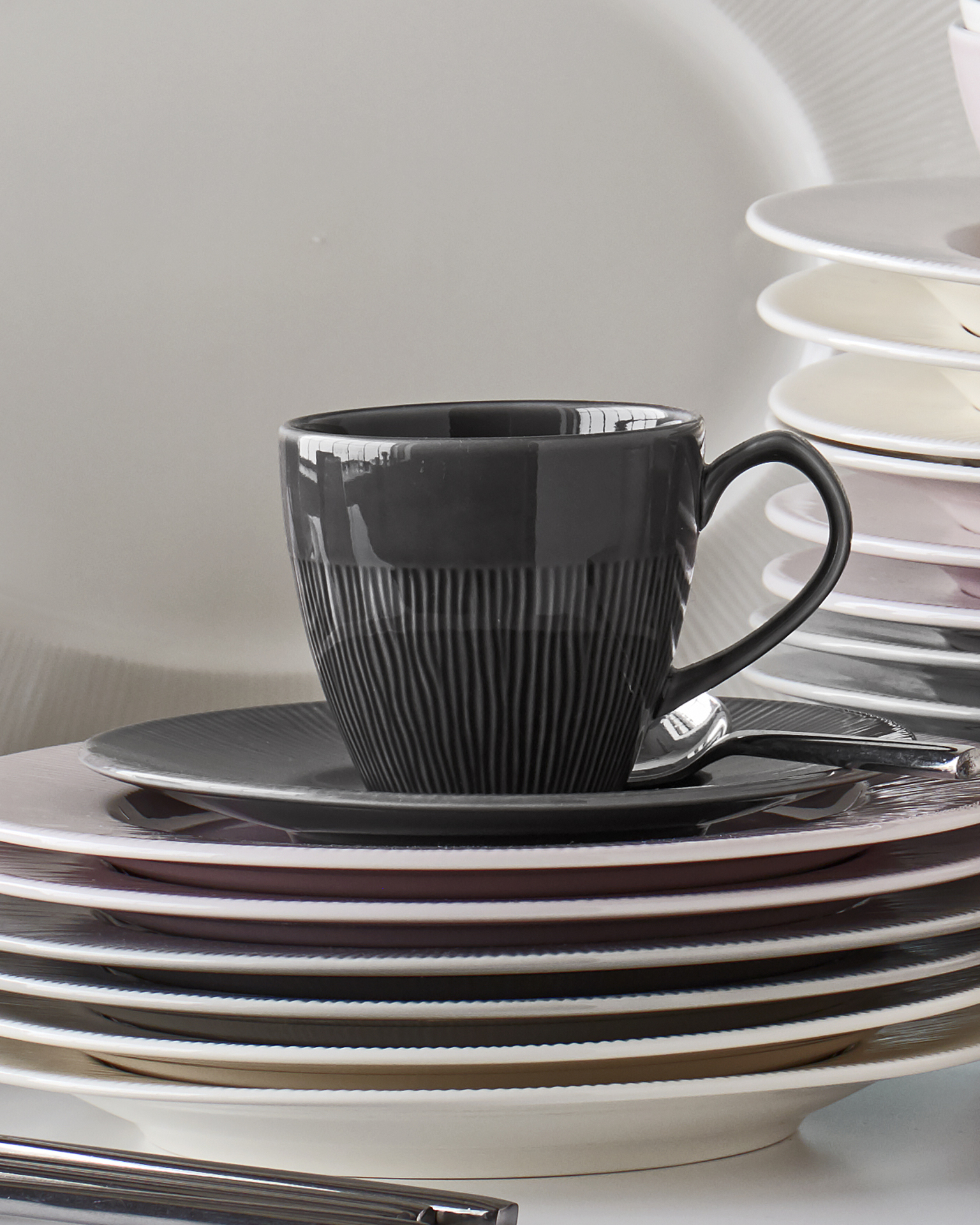 På en trave tallrikar i olika färger står en kopp och fat från servisen Colormix.