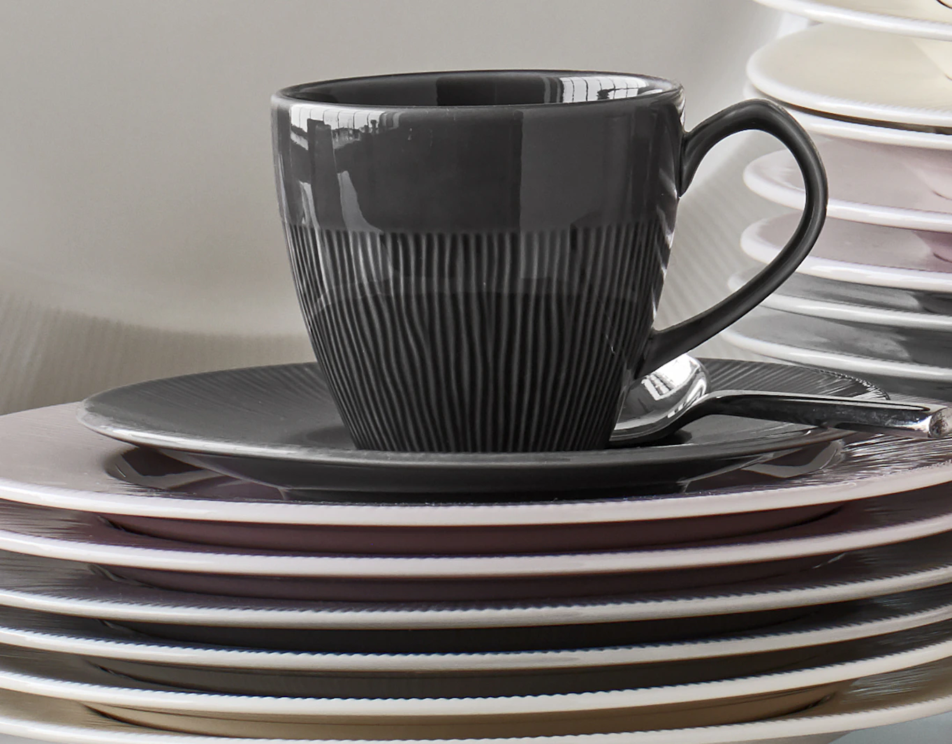 På en trave tallrikar i olika färger står en kopp och fat från servisen Colormix.