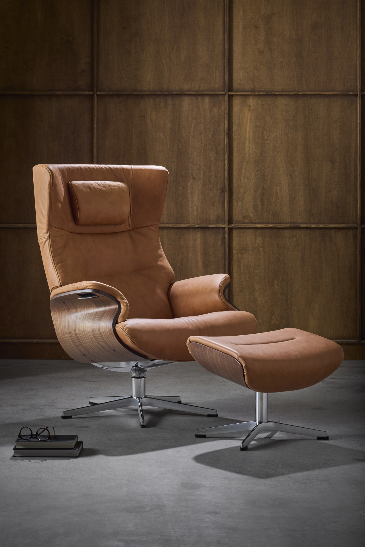 En brun skinnsfåtölj med underrede i valnöt står bredvid en fotpall