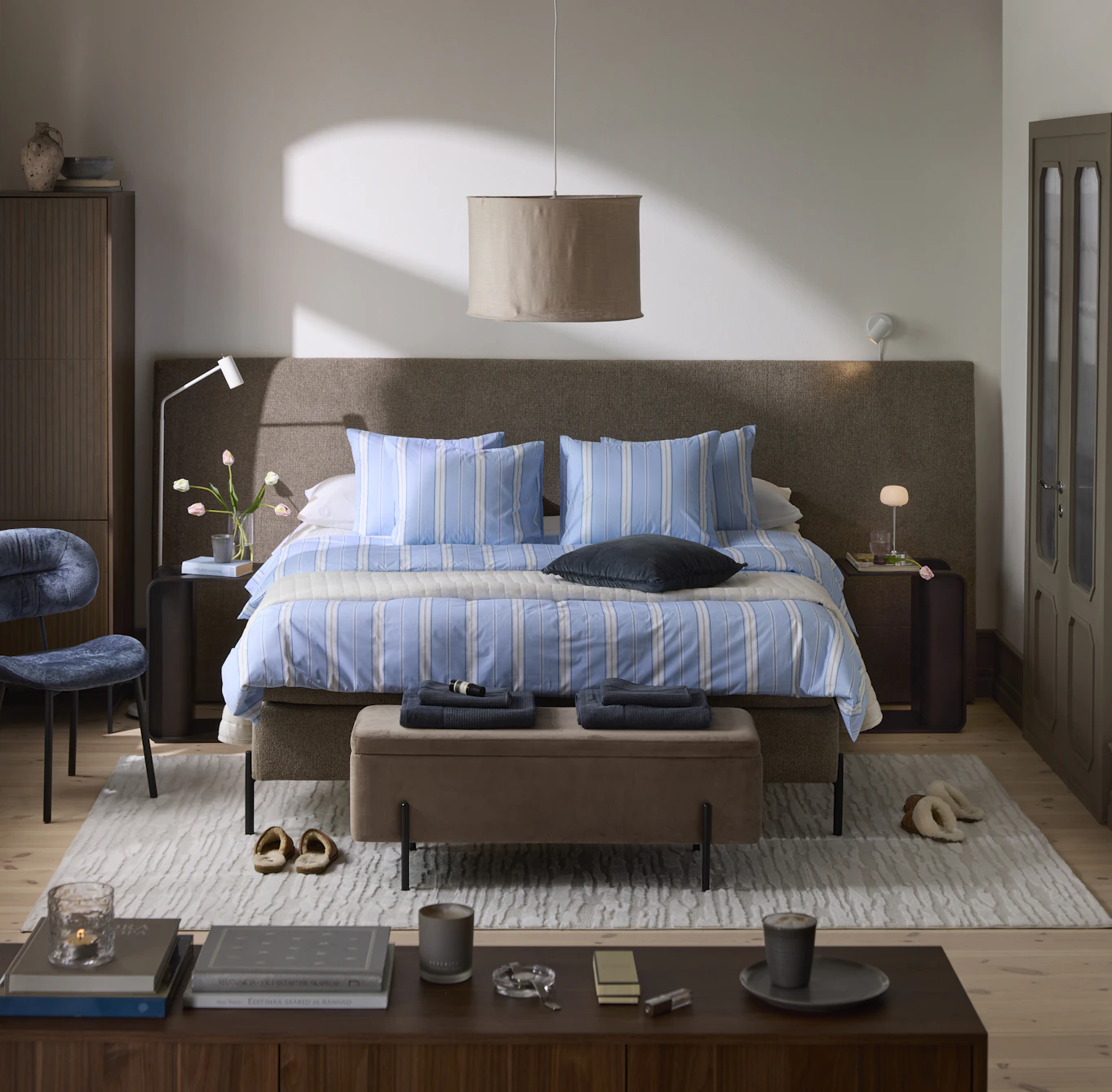 Sovrumsmiljö med stor säng i perspektiv framifrån och en extra bred mörkgrå gavel som går långt utanför sängens bredd. 
