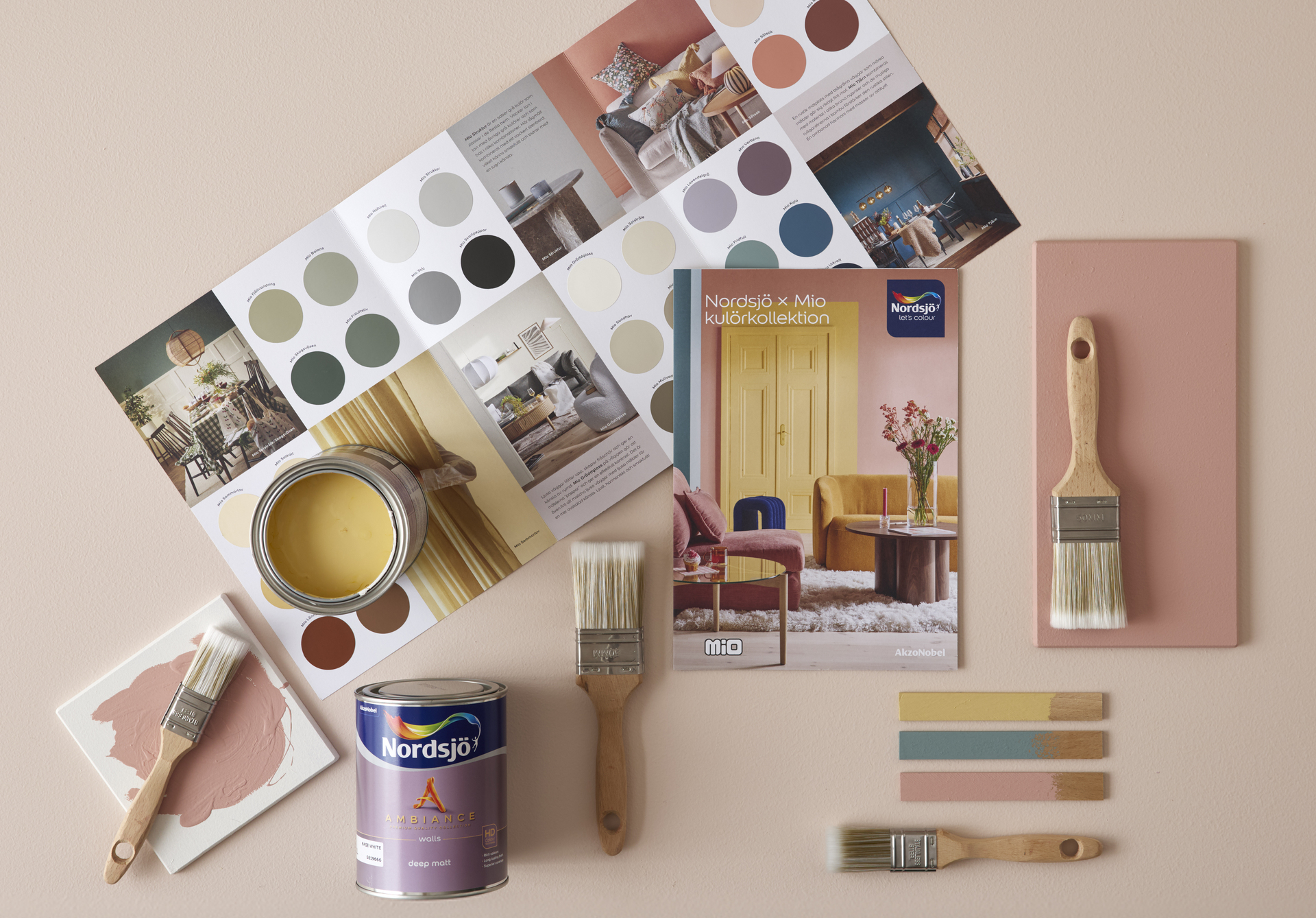Penslar och färgburkar ligger på golvet ihop med en färgkarta från färgföretaget Nordsjö. 