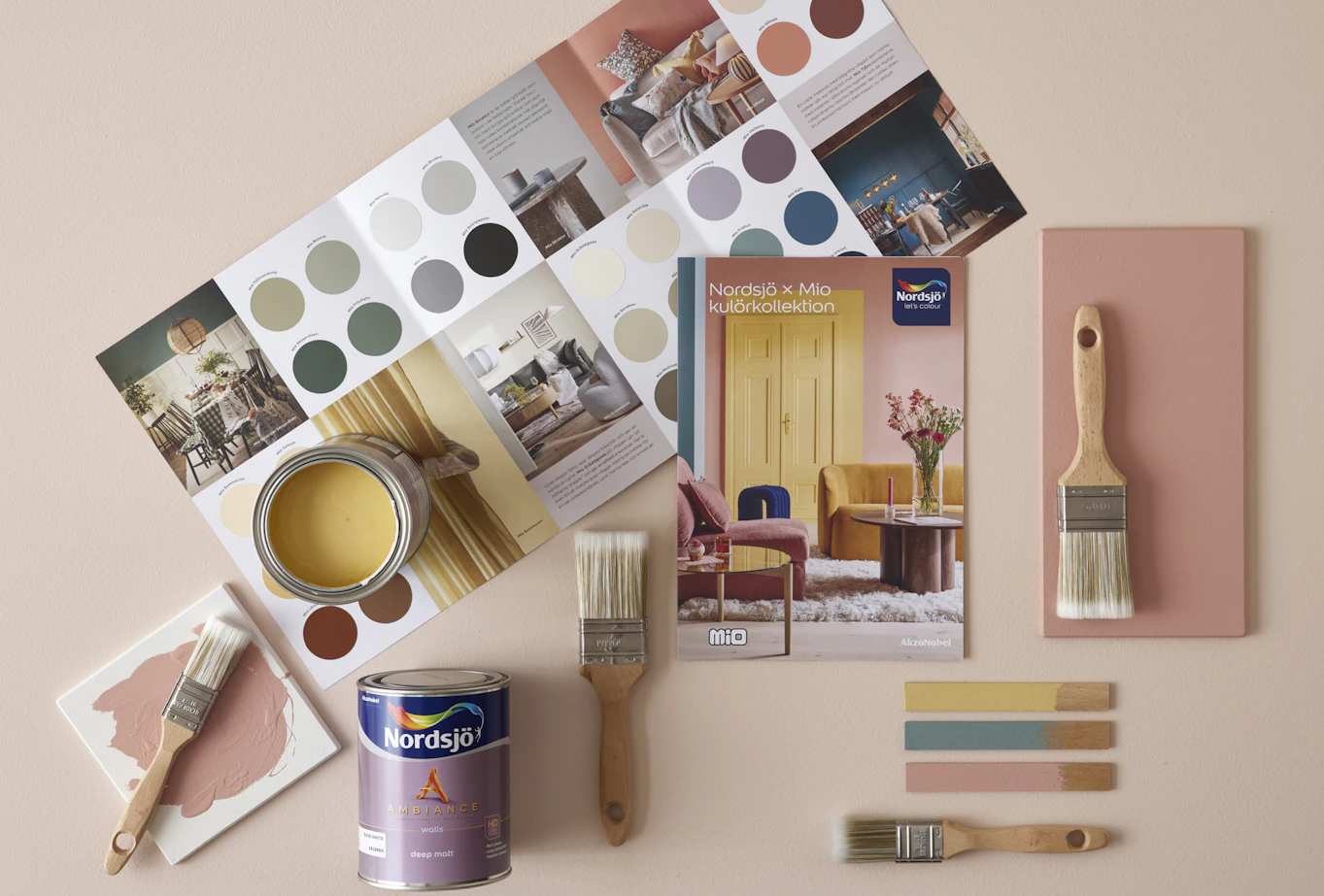 Penslar och färgburkar ligger på golvet ihop med en färgkarta från färgföretaget Nordsjö.