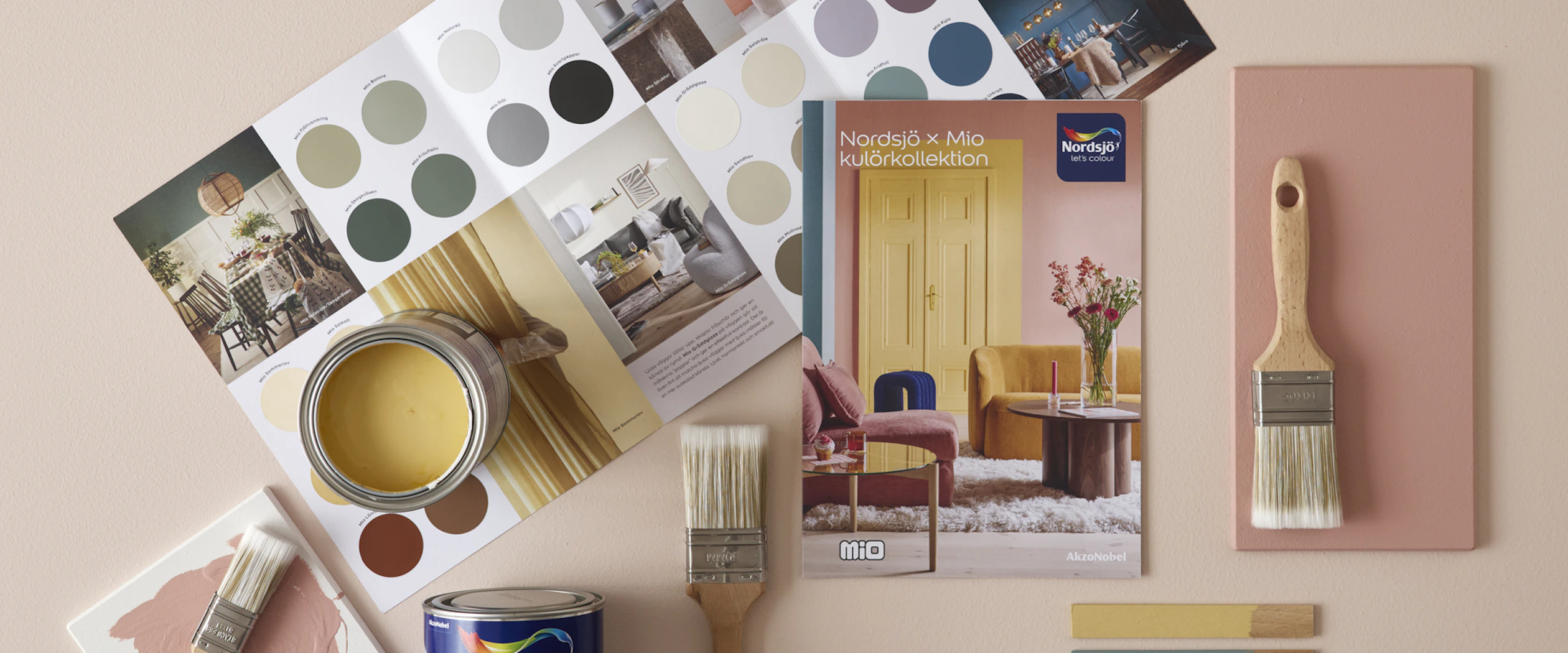 Penslar och färgburkar ligger på golvet ihop med en färgkarta från färgföretaget Nordsjö.