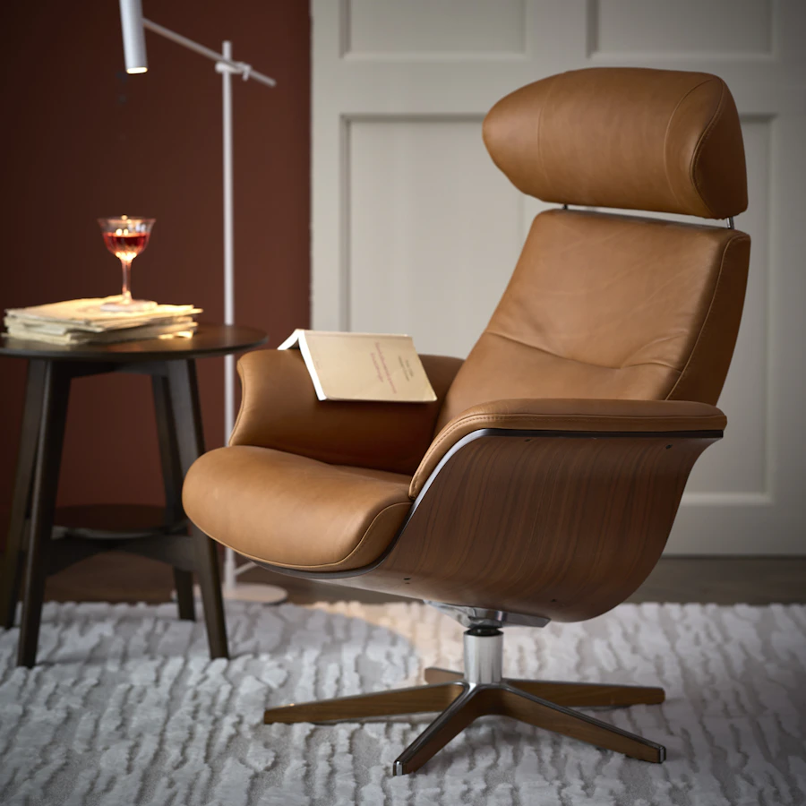 I ett rum med vit bröstpanel står en konjaksfärgad skinnfåtölj med underrede i valnöt brevid ett sidobord