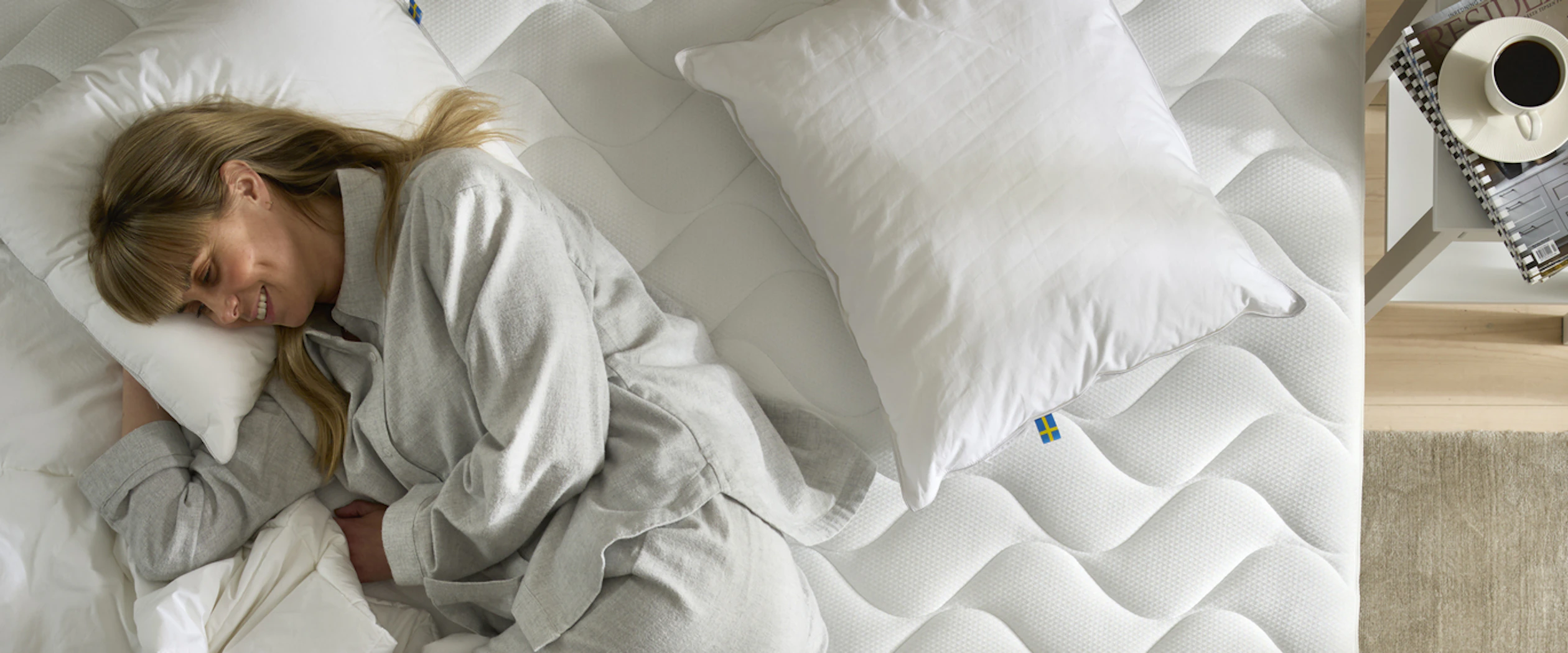 En kvinna ligger med armen under en huvudkudde i en obäddad säng.