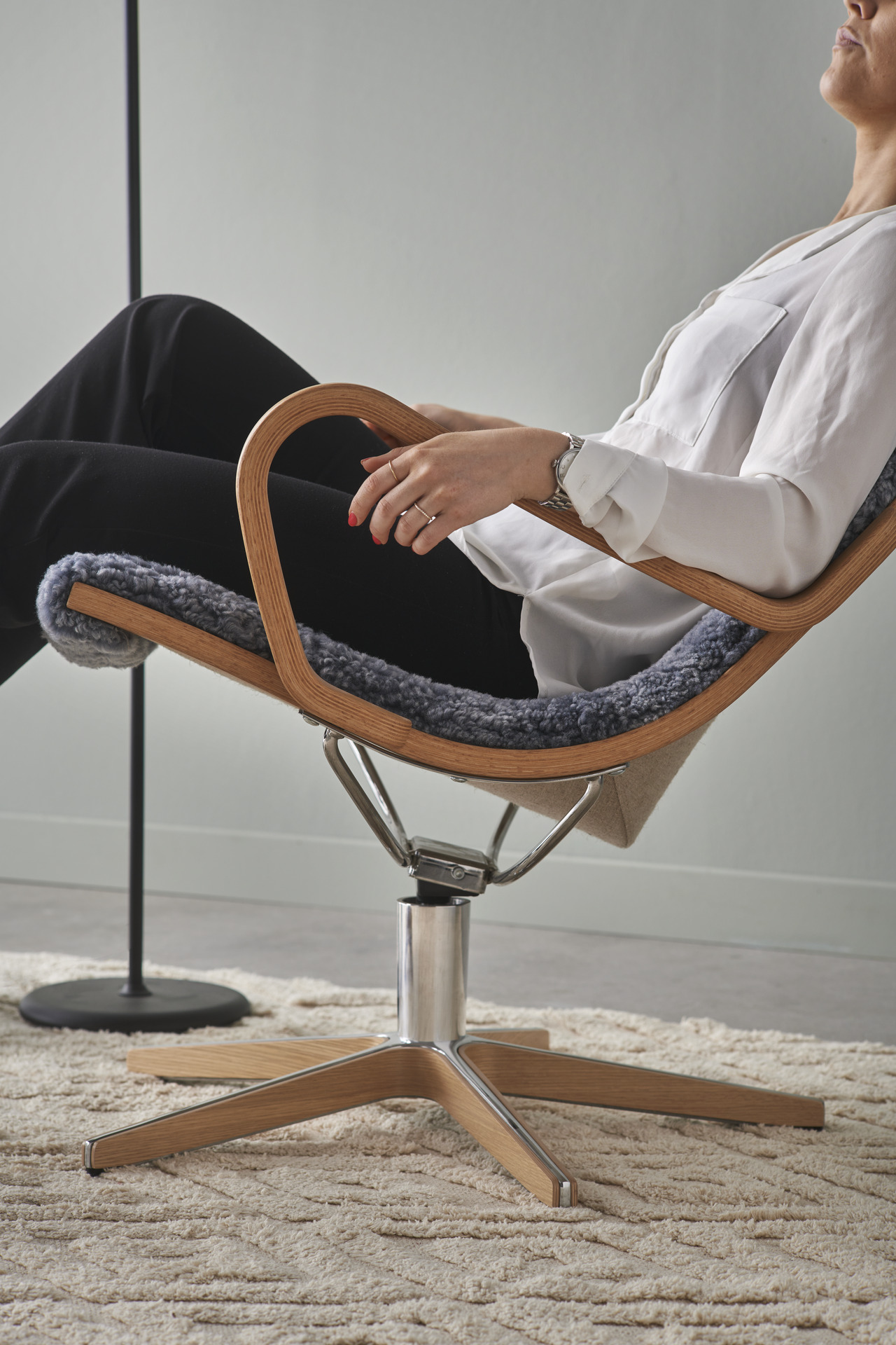 I en grå fårskinnsfåtölj med detaljer i ek lutar sig en person bakåt