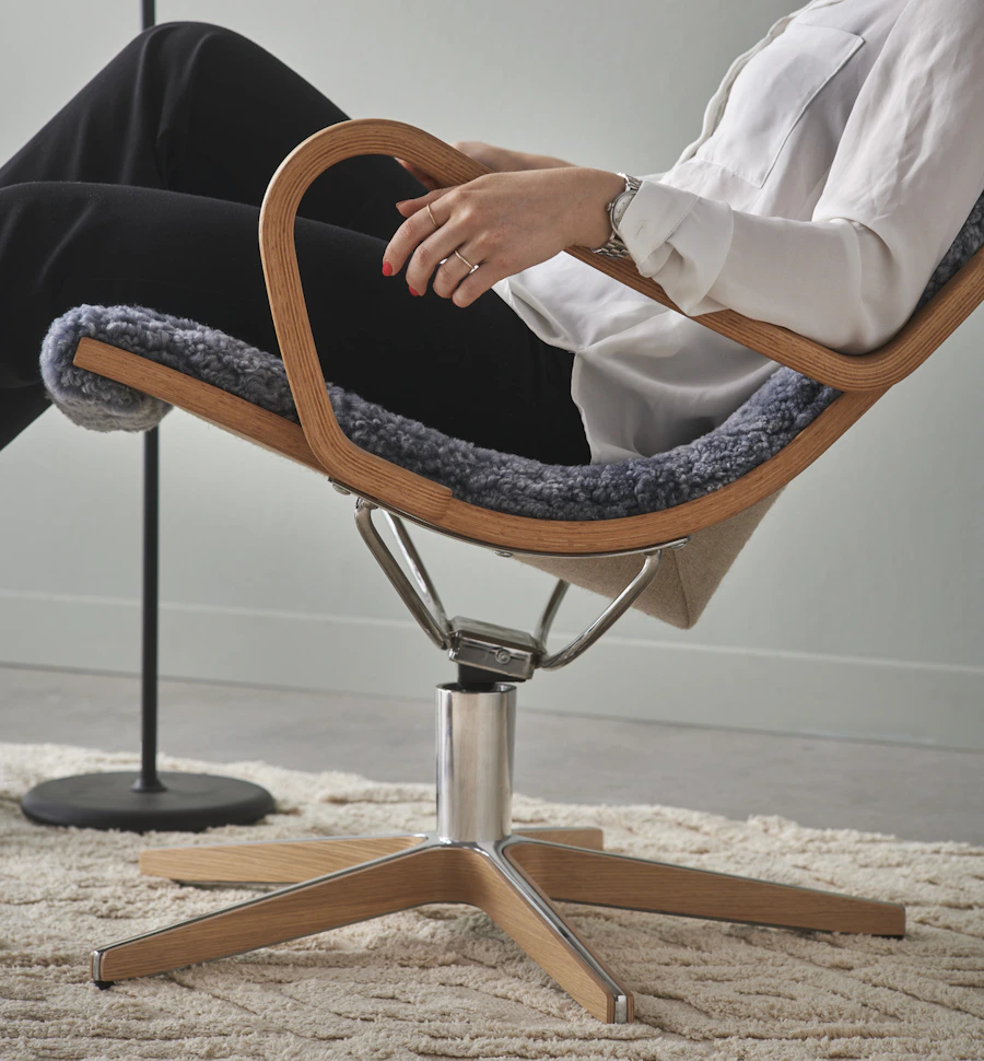 I en grå fårskinnsfåtölj med detaljer i ek lutar sig en person bakåt
