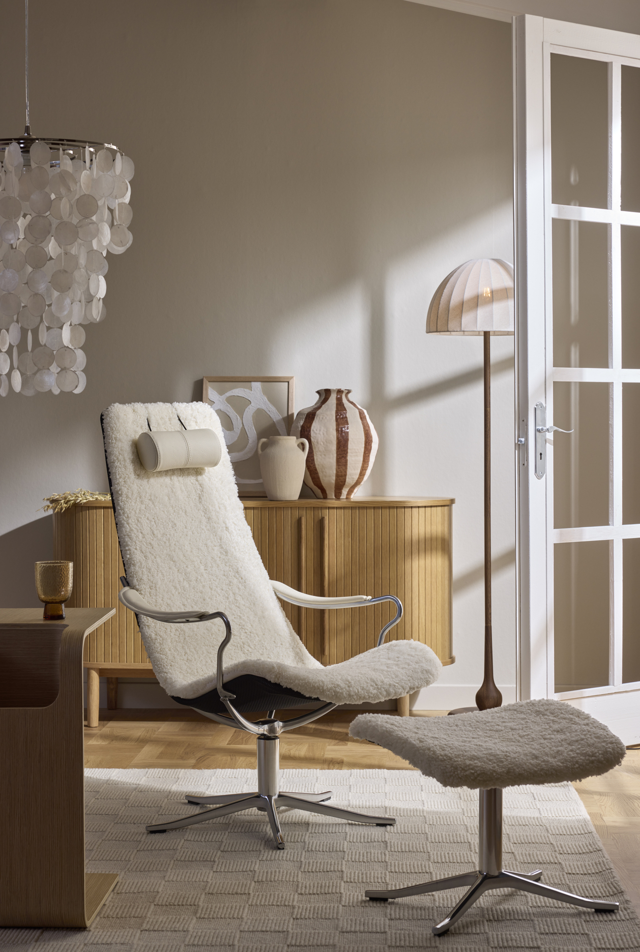 I ett beiget rum står en vit fåtölj i fårskinn framför en ekfärgad skänk