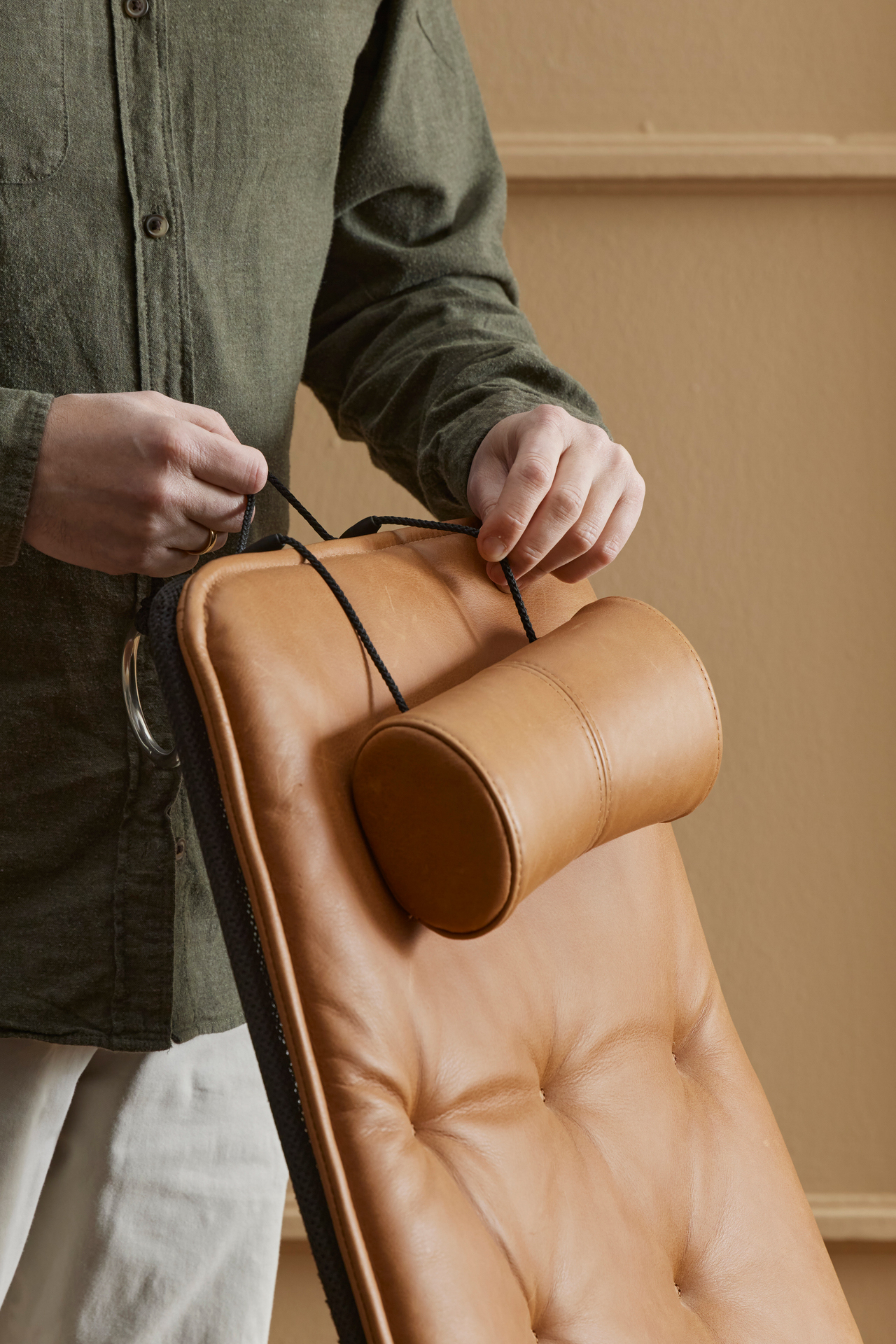 Närbild på en brun läderfåtölj, två händer rättar till tackkudden