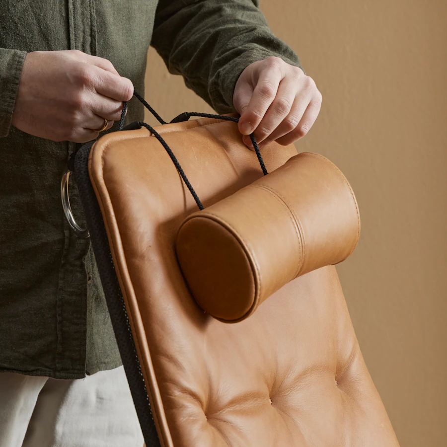 Närbild på en brun läderfåtölj, två händer rättar till tackkudden