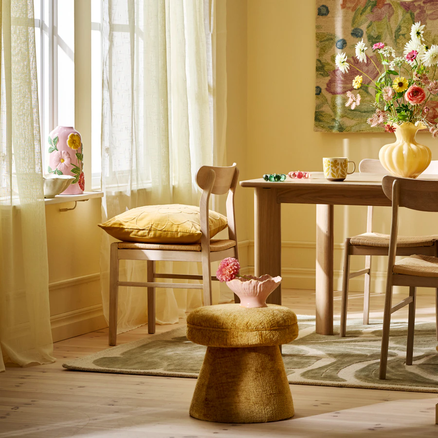 Ljus sipprar in genom tunna gardiner in i rum med gula väggfärger med matbord med trendig vas med blommor i.