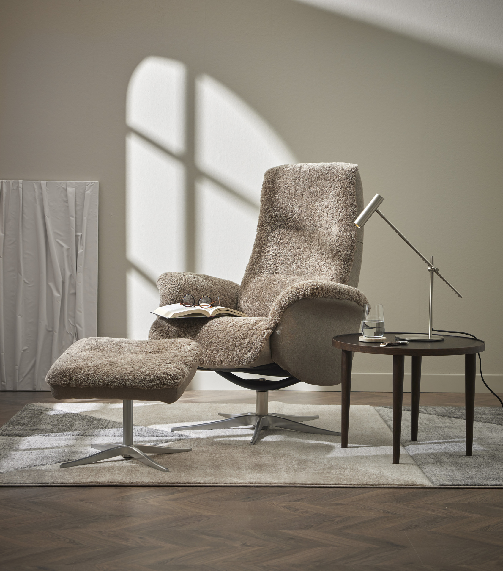 I ett rum står en beige fårskinnsfåtölj bredvid ett sidobord i valnöt