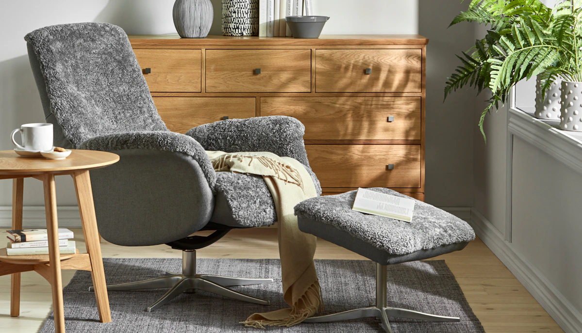 Framför en byrå i ek står en grå fårskinnsfåtölj som är lätt lutad bakåt