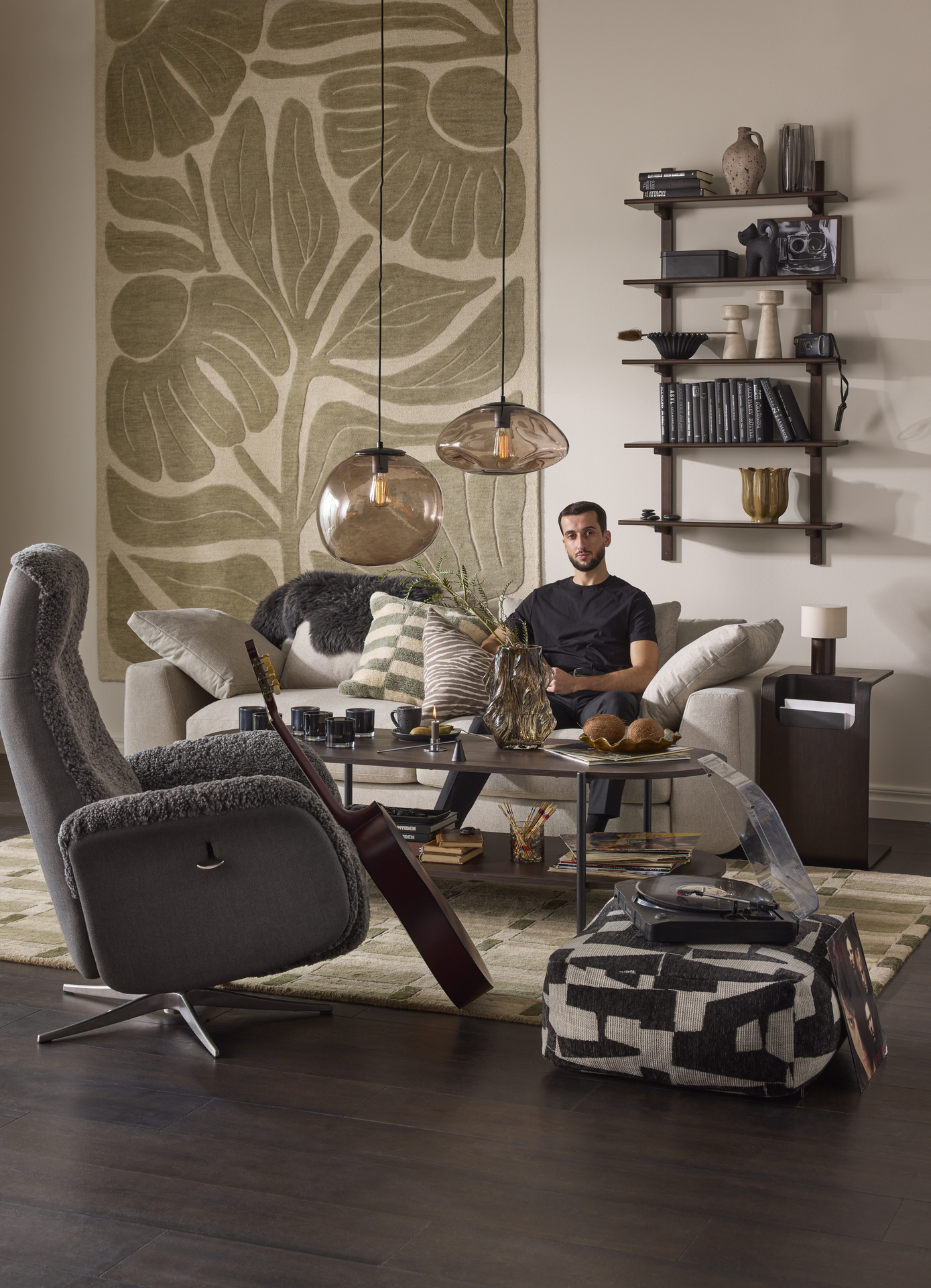 Vardagsrumsmiljö med fåtölj i förgrunden, i bakgrunden sitter en man i ljusgrå soffa. 