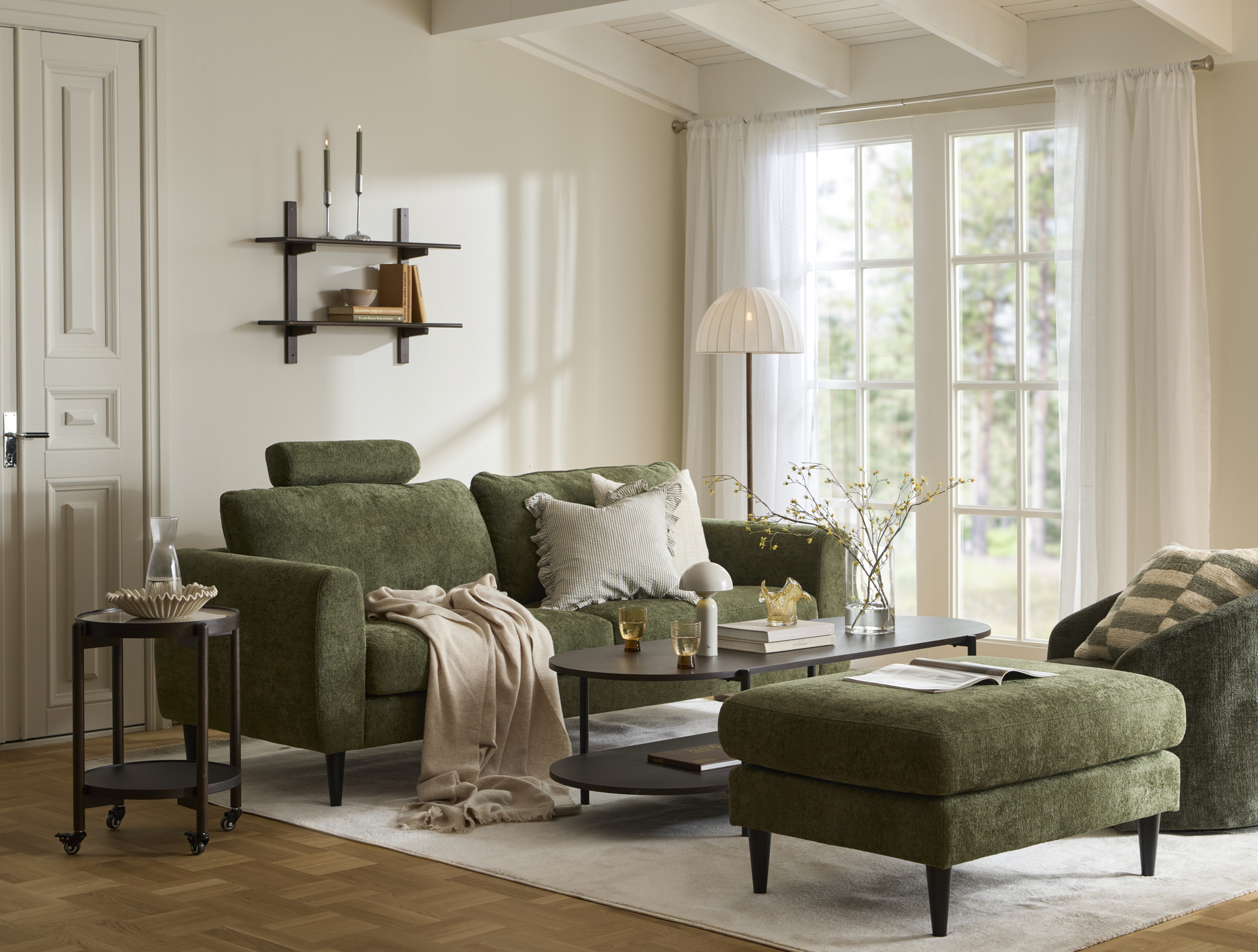 I ett ljust vardagsrum står en grön soffa vid ett soffbord i mörkt trä. Intill står en grön fotpall och en grön fåtölj