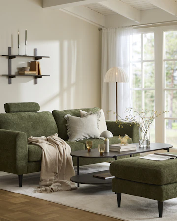 I ett ljust vardagsrum står en grön soffa vid ett soffbord i mörkt trä. Intill står en grön fotpall och en grön fåtölj