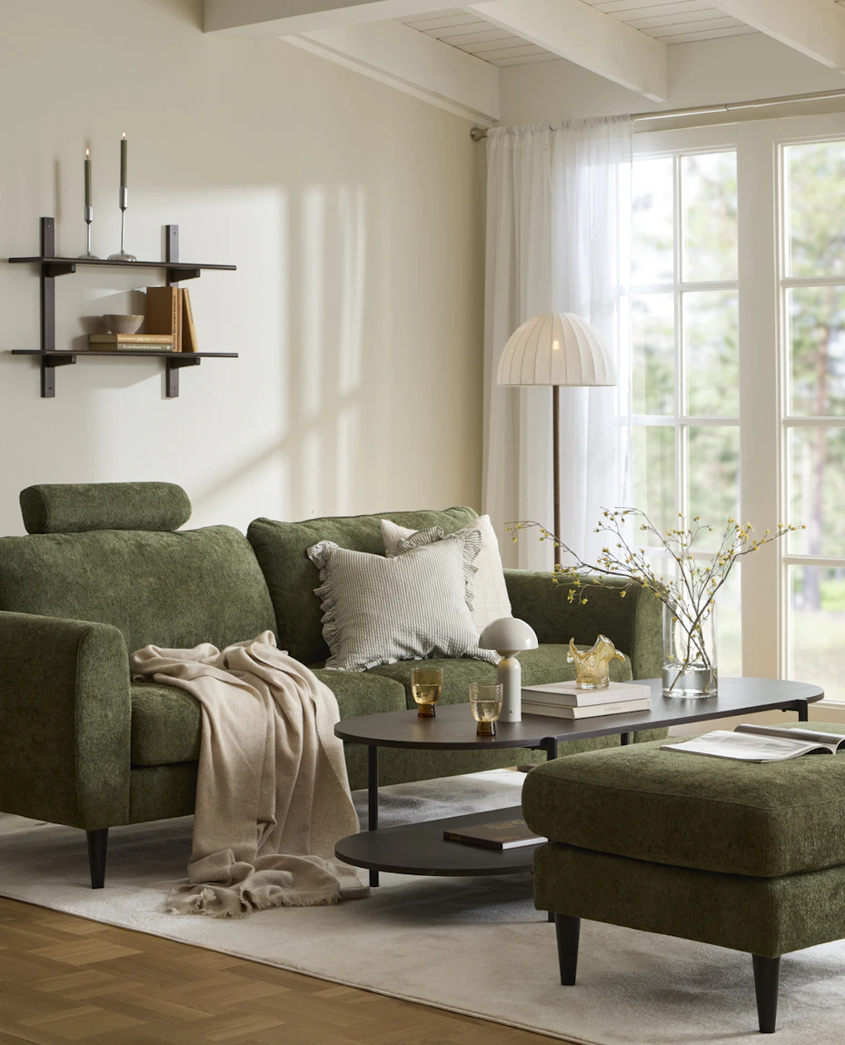 I ett ljust vardagsrum står en grön soffa vid ett soffbord i mörkt trä. Intill står en grön fotpall och en grön fåtölj