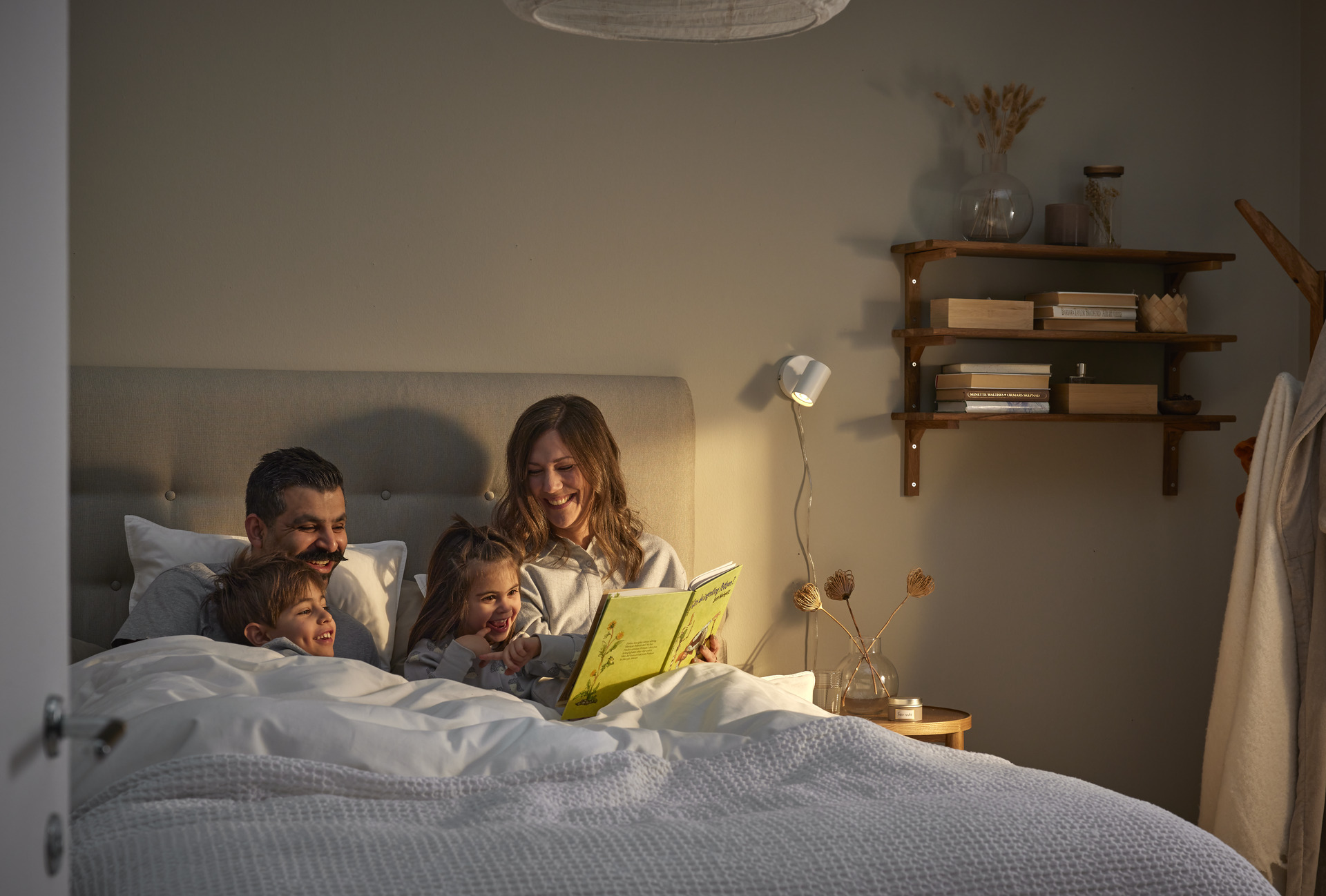 en familj sitter nedbäddad i en säng och läser en bok tillsammans