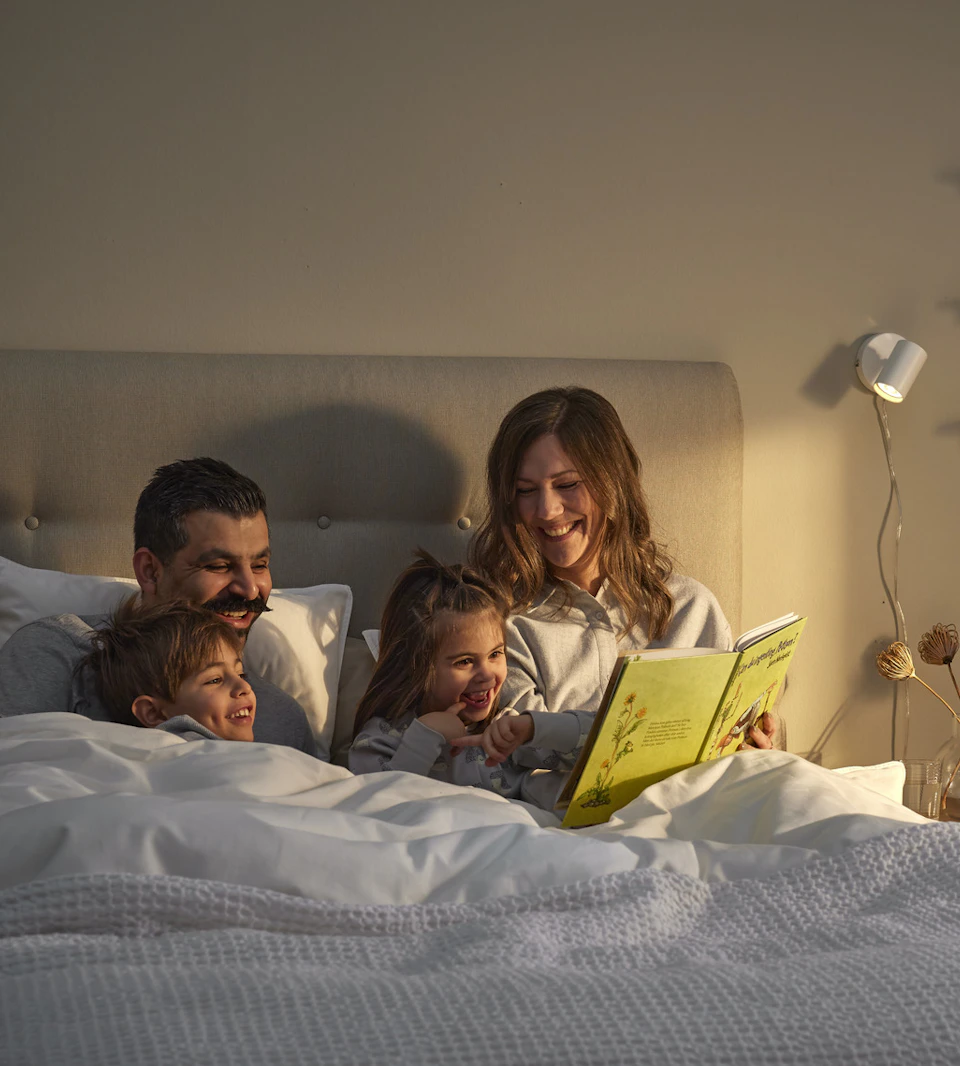 en familj sitter nedbäddad i en säng och läser en bok tillsammans