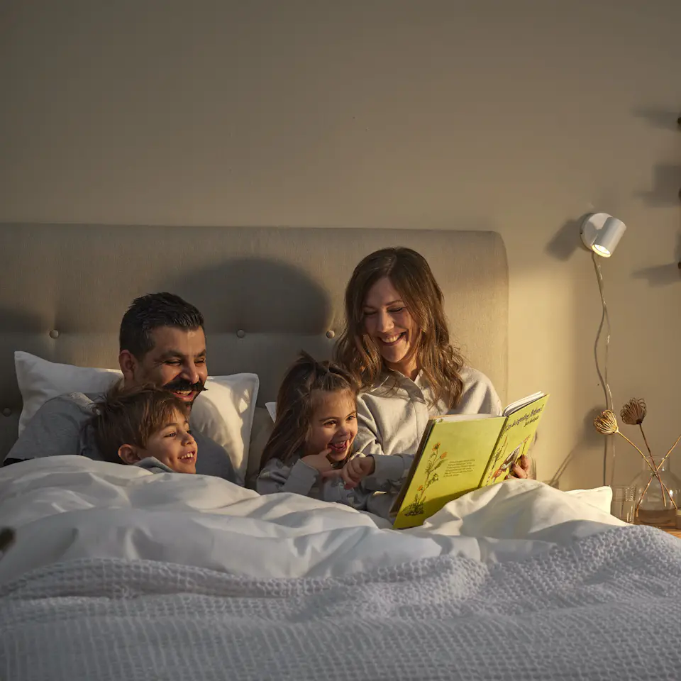 en familj sitter nedbäddad i en säng och läser en bok tillsammans