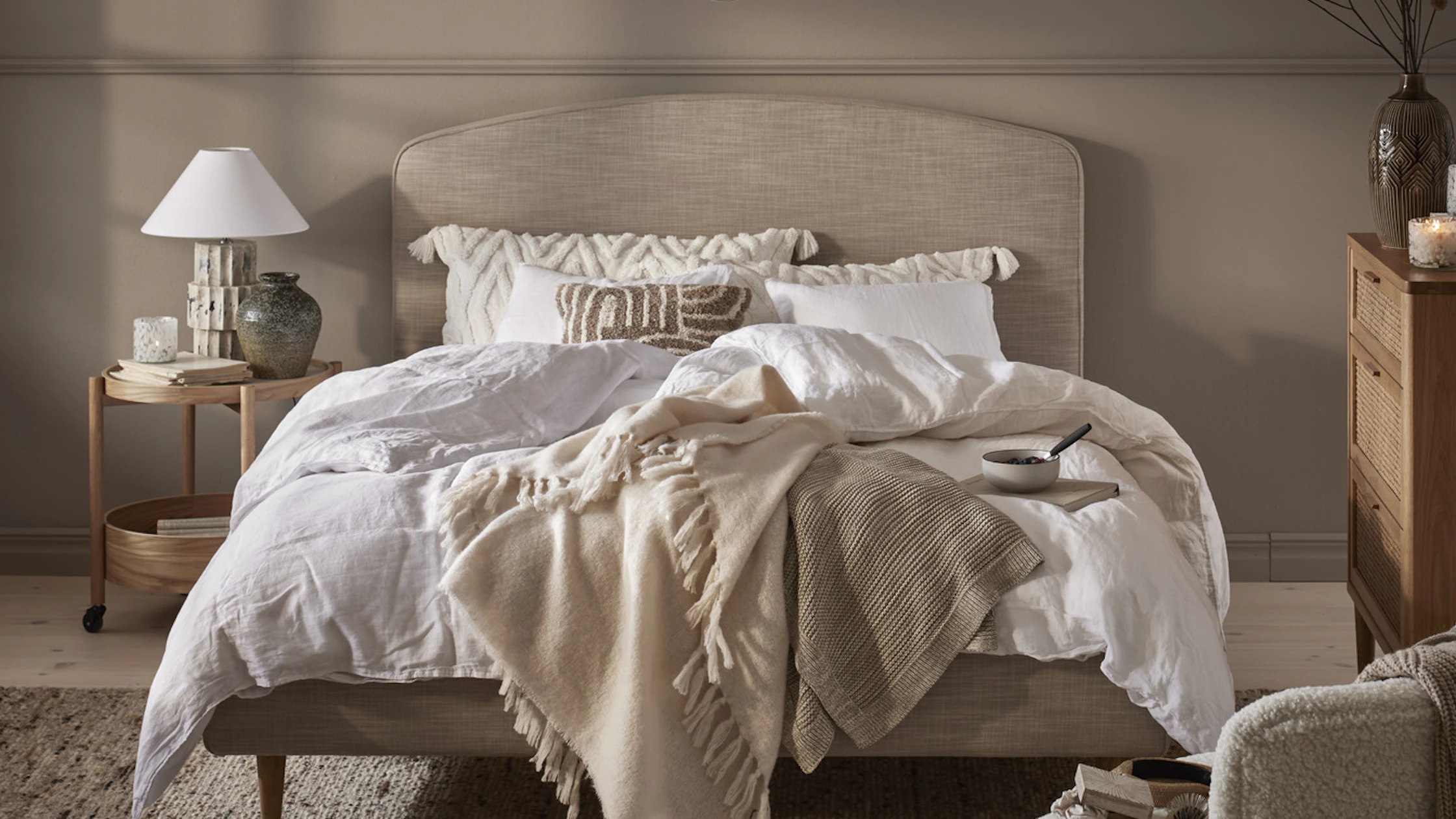 en beige säng bäddad med vita lakan i ett sovrum