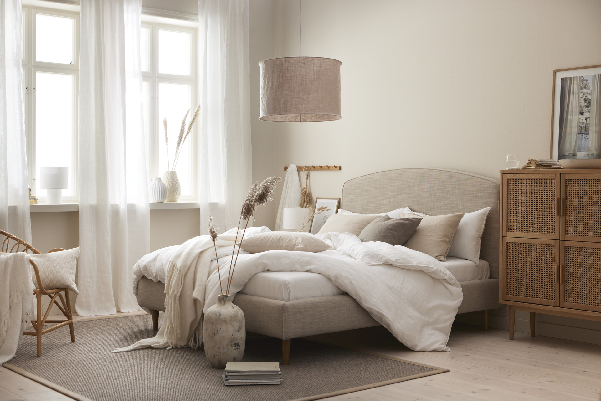 en beige säng bäddad med vita lakan står i ett ljust sovrum 