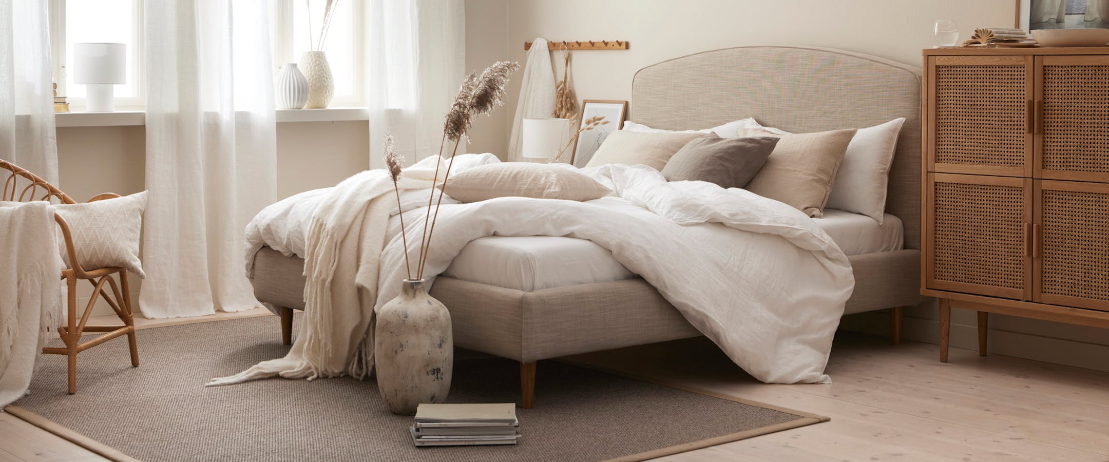 en beige säng bäddad med vita lakan står i ett ljust sovrum