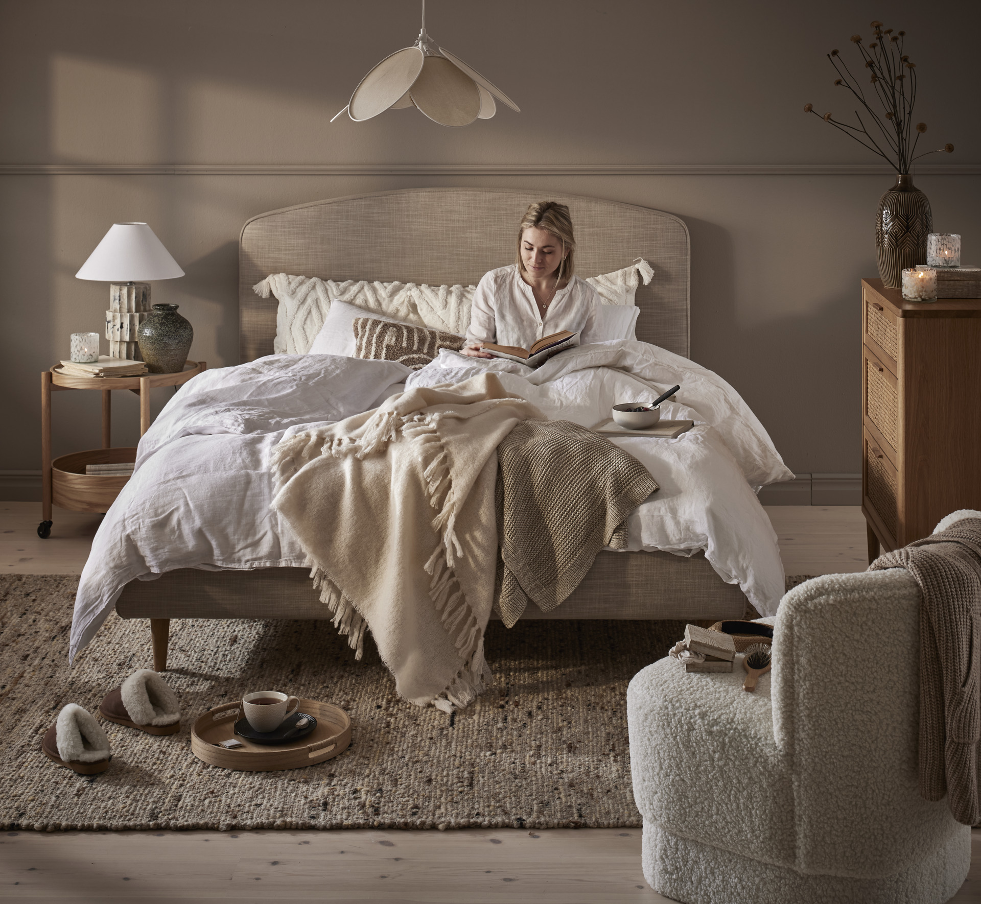 en tjej sitter i en bäddad beige säng i ett sovrum i dova toner