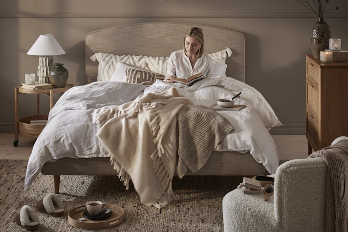 en tjej sitter i en bäddad beige säng i ett sovrum i dova toner