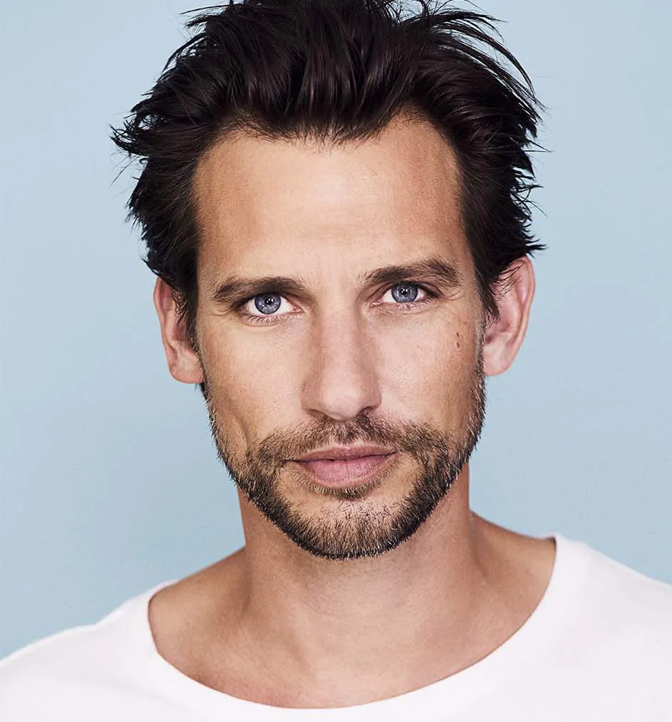 en brunhårig man med skägg tittar in i kameran