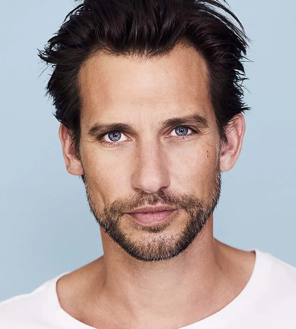 en brunhårig man med skägg tittar in i kameran