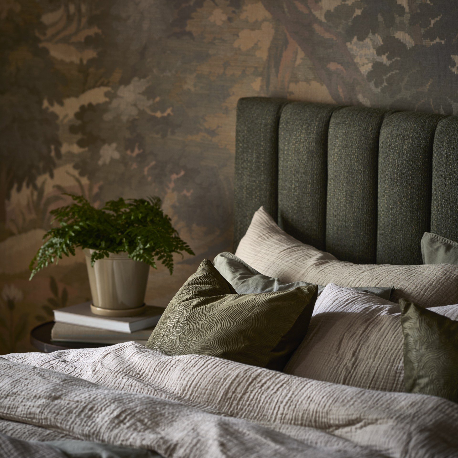 en säng med grön sänggavel och grå och bruna sängkläder står i ett sovrum med en mönstrad grön tapet