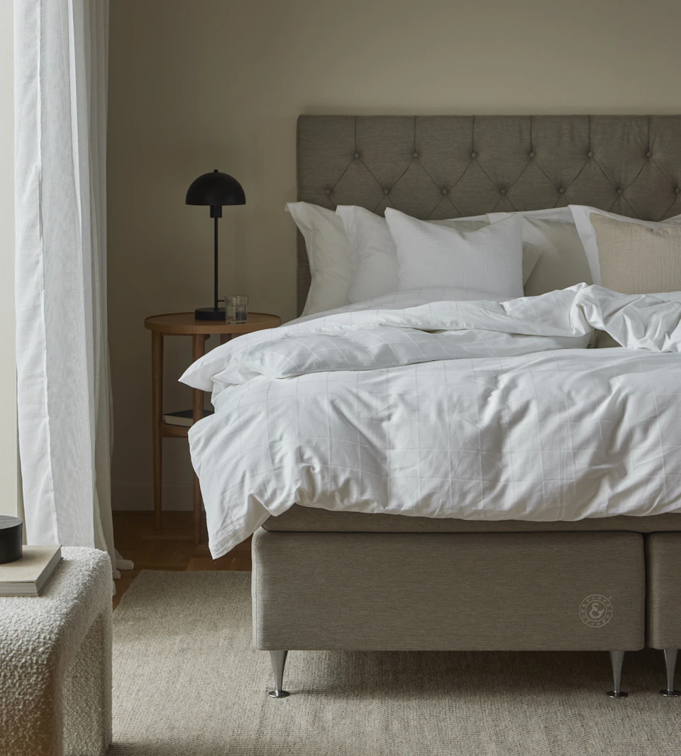 en grå kontinentalsäng med pikerad gavel står i ett sovrum med beiga väggar
