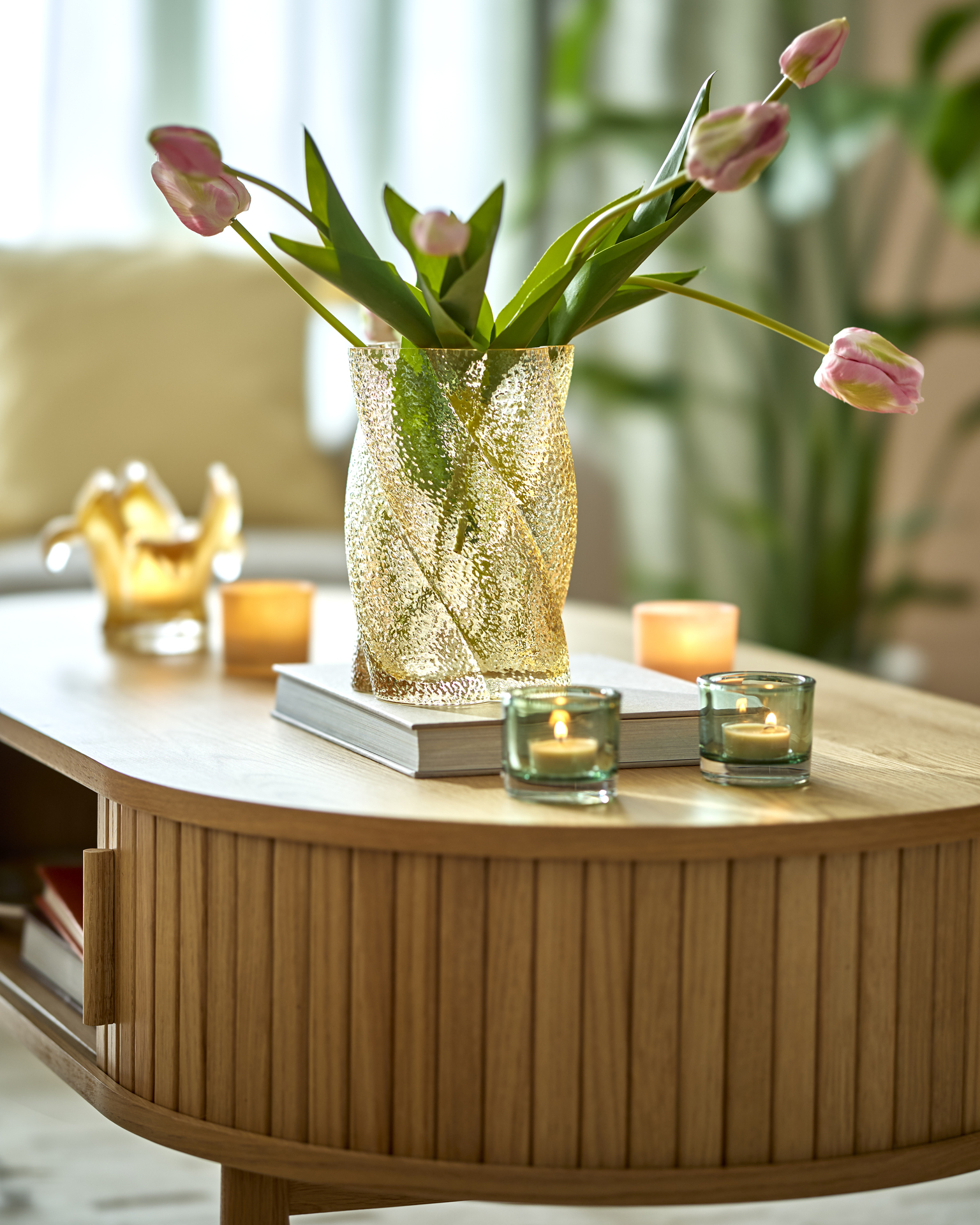 ett rektangulärt soffbord med rundade kanter står i ett vardagsrum. På bordet finns dekoration som ljuslyktor, en bok och vas med blommor.