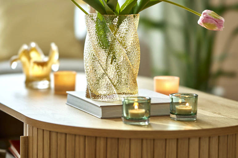 ett rektangulärt soffbord med rundade kanter står i ett vardagsrum. På bordet finns dekoration som ljuslyktor, en bok och vas med blommor.