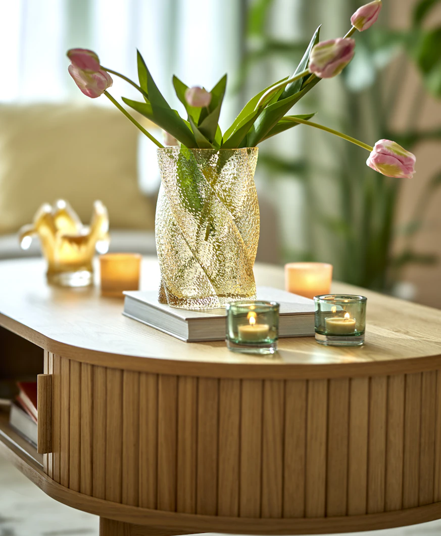 ett rektangulärt soffbord med rundade kanter står i ett vardagsrum. På bordet finns dekoration som ljuslyktor, en bok och vas med blommor.