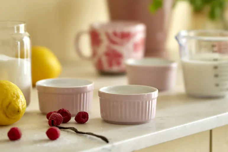På en köksbänk full med redskap för bakning står två små rosa formar.